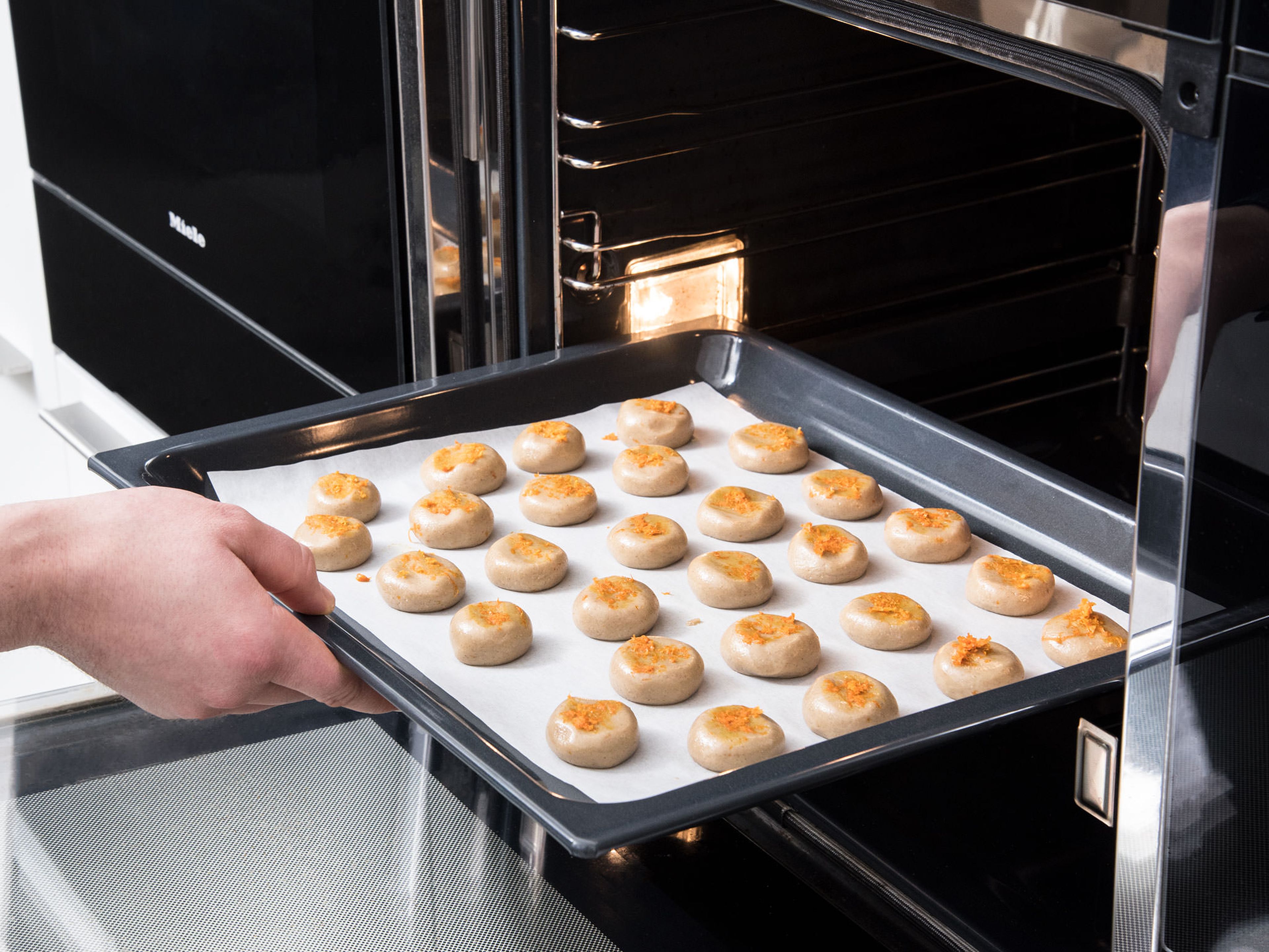 Form the dough into small balls (2 cm/0.8 in). Place them onto a parchment-lined baking sheet and press to flatten them slightly. Sprinkle remaining orange zest on top, and bake at 180°C/350°F for approx. 10 min. Enjoy!