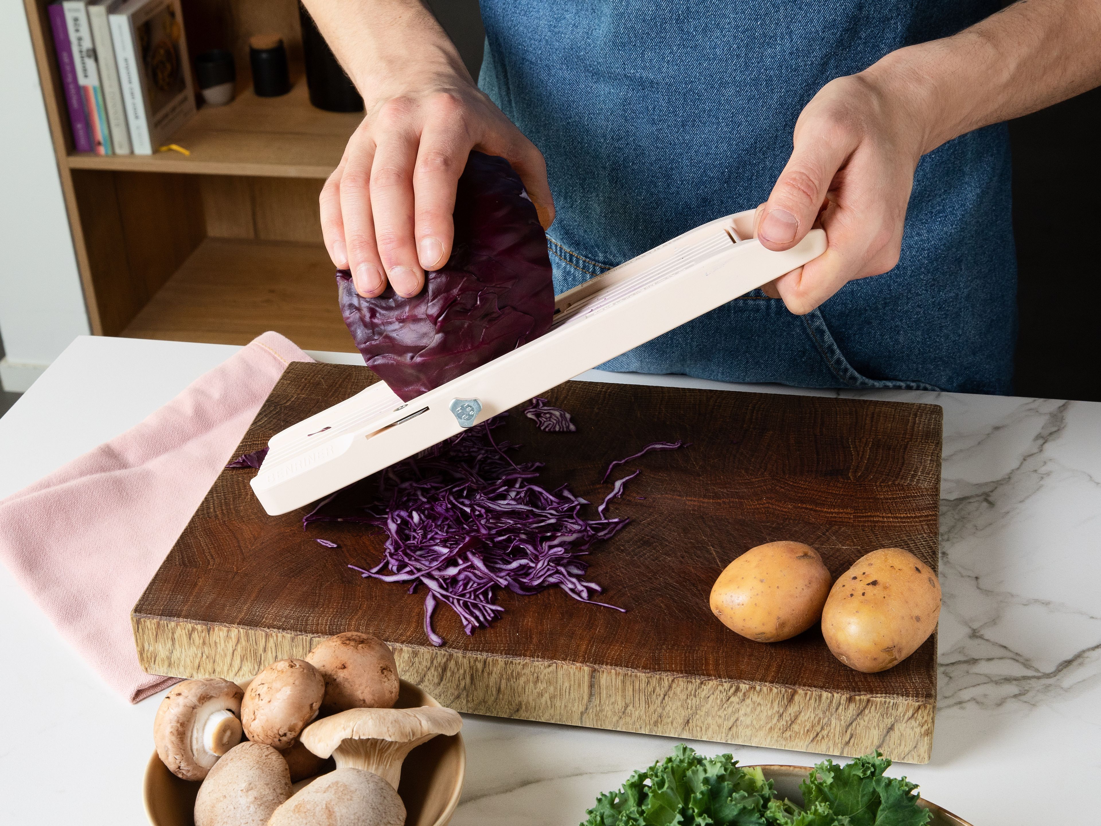Den Backofen auf 200 °C (Ober-/Unterhitze) vorheizen. Den Strunk des Rotkohls entfernen und fein hobeln. Kartoffel schälen und ebenfalls raspeln. Zwiebel und Knoblauchzehen schälen und fein hacken. Beim Grünkohl, die Blätter vom Strunk lösen und grob hacken. Pilze putzen und in mundgerechte Stücke schneiden. Petersilie fein hacken.