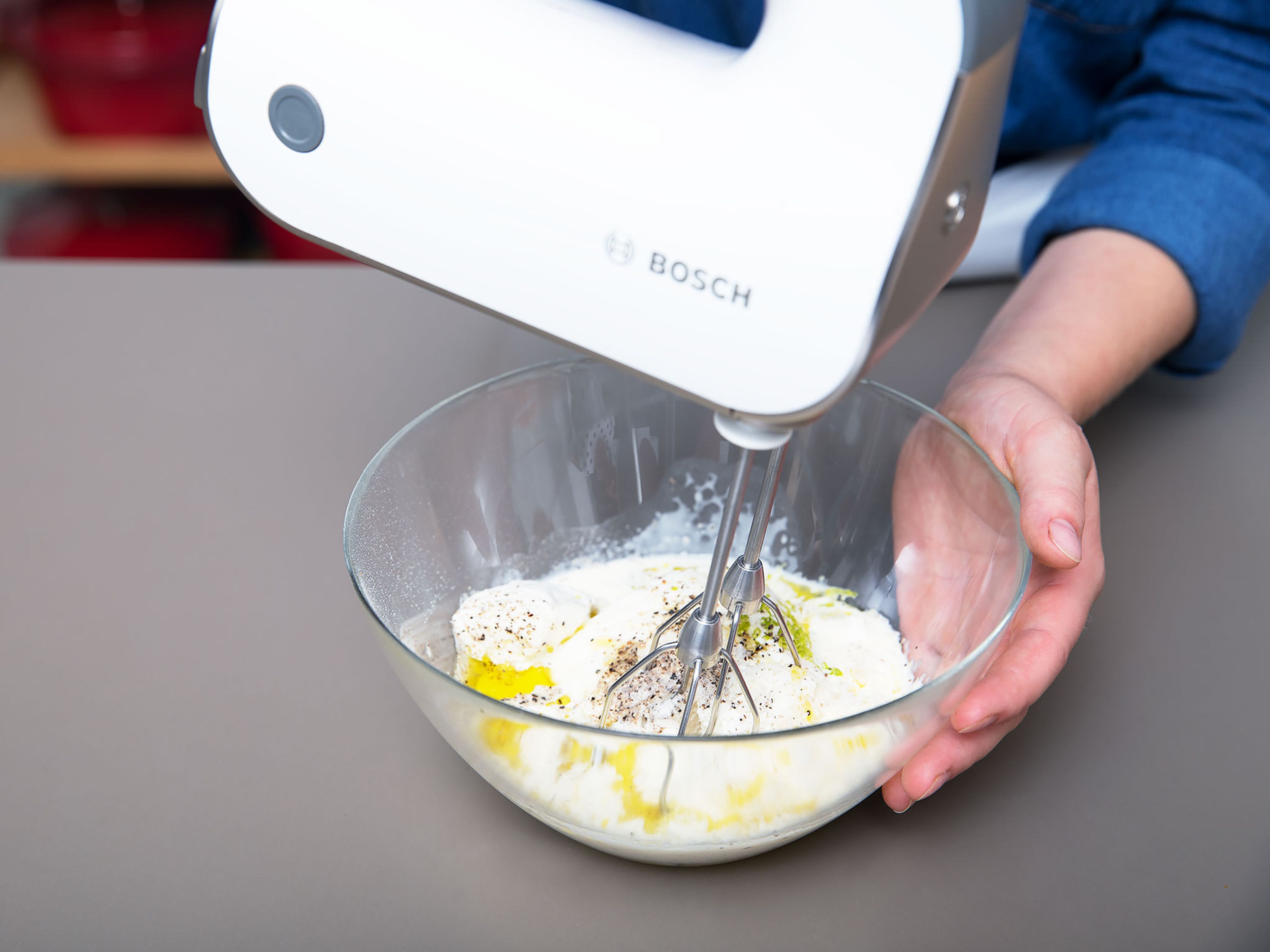 Peel and finely chop garlic. Zest and juice the lime. Add ricotta cheese, egg, heavy cream, chopped garlic, freshly grated Parmesan cheese, half of the lime zest, and remaining olive oil to a bowl and use a hand mixer to stir to combine. Season with salt and pepper to taste.