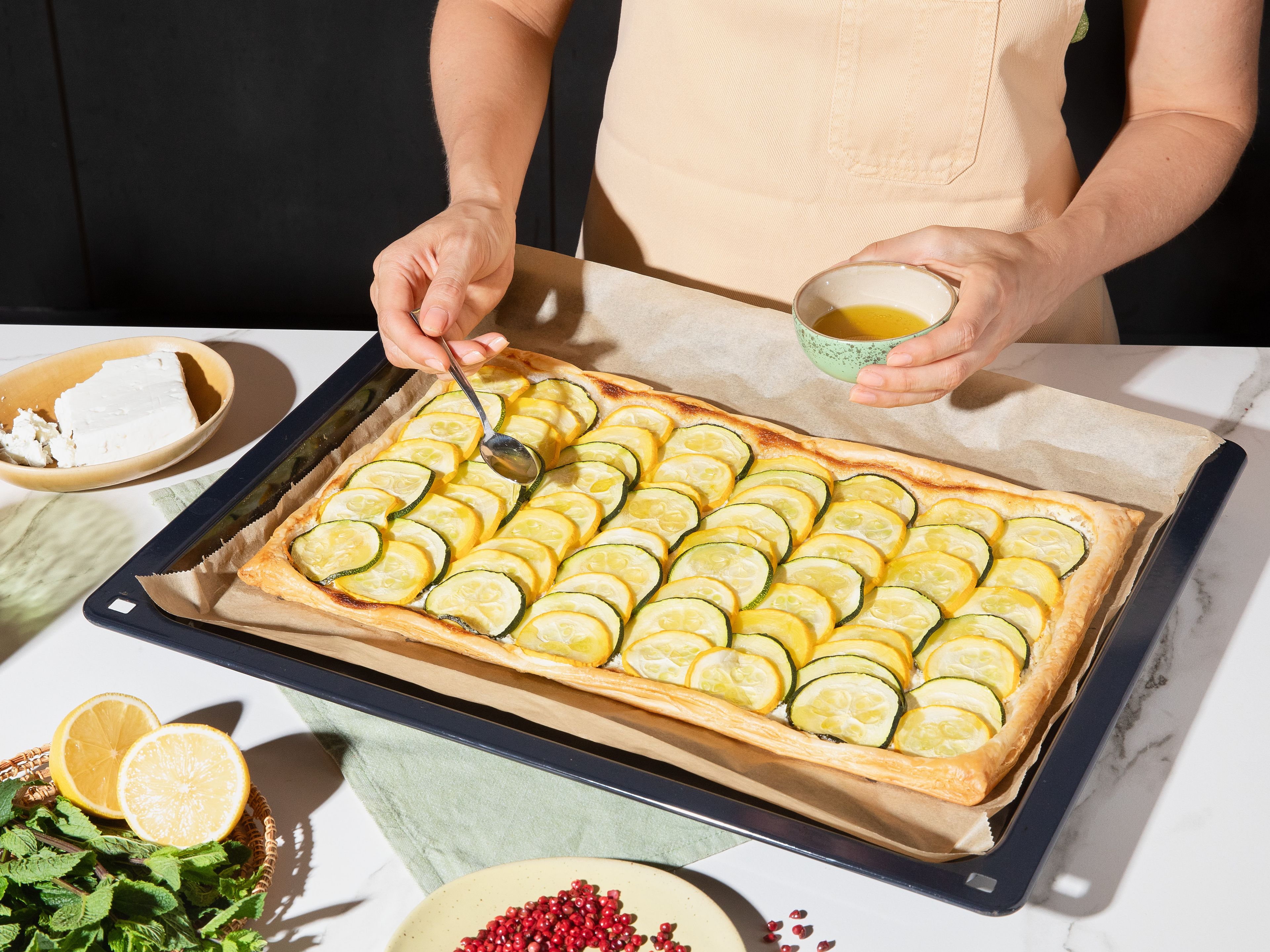 Finally, mix honey with lemon juice and olive oil. Drizzle honey-lemon mixture over warm tart and garnish with remaining crumbled feta, fresh mint, crushed pink peppercorns, and lemon zest before serving.
