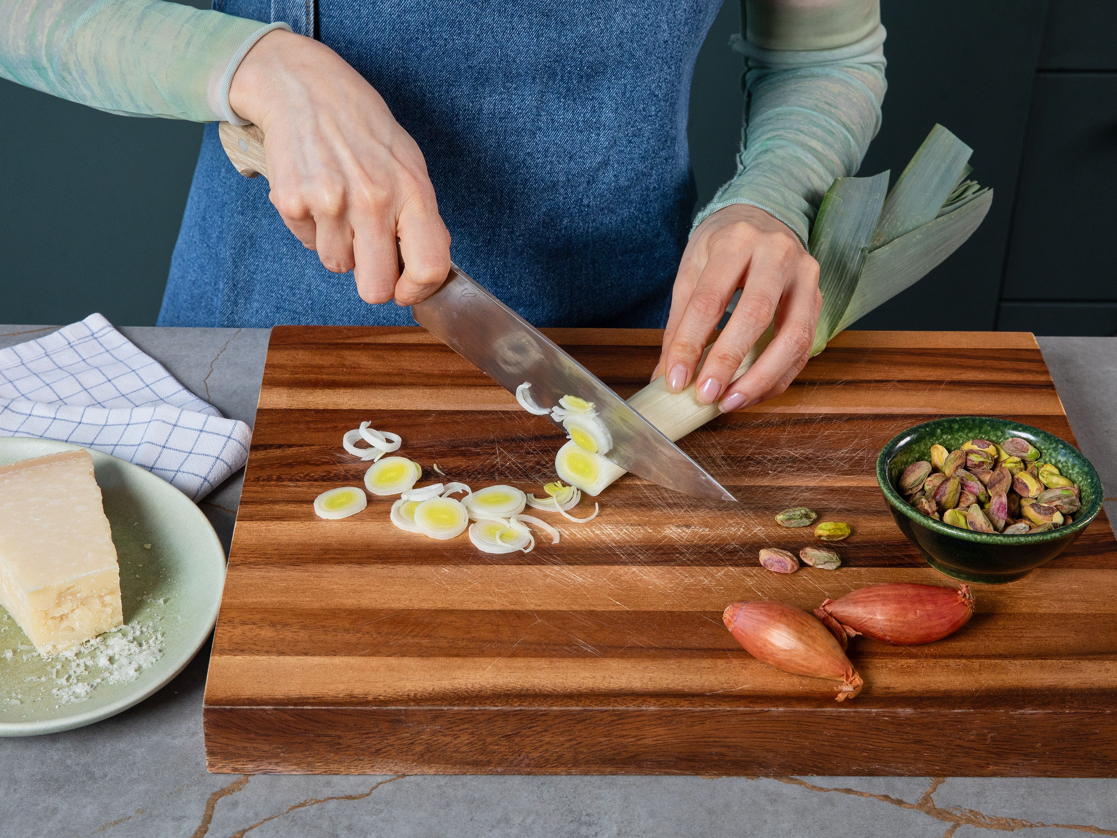 Die Schalotte schälen und in feine Würfel schneiden, den Lauch putzen und in feine Ringe schneiden. Den Parmesan reiben und Pistazien grob hacken. Die Butter und etwas Olivenöl in einer großen Pfanne bei mittlerer Hitze schmelzen lassen. Die Schalotte und Lauch hinzufügen und ca. 3-4 Min. anschwitzen, bis sie weich und glasig sind.