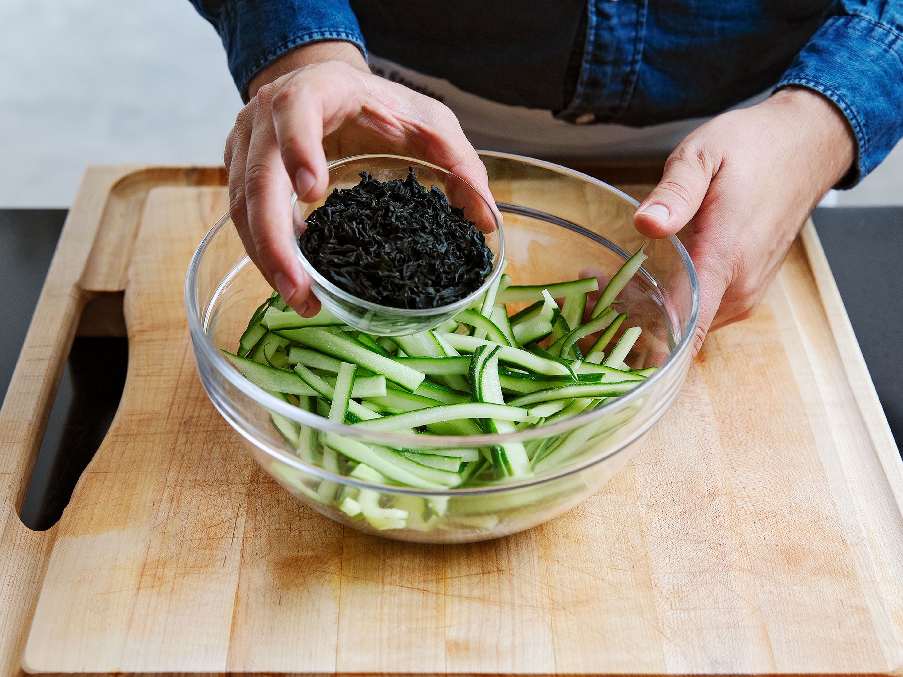 Gurken für den Salat in dünne Streifen schneiden und in eine Schüssel geben. Die Hälfte des Salzes und Wakame Algen dazugeben und vermengen.