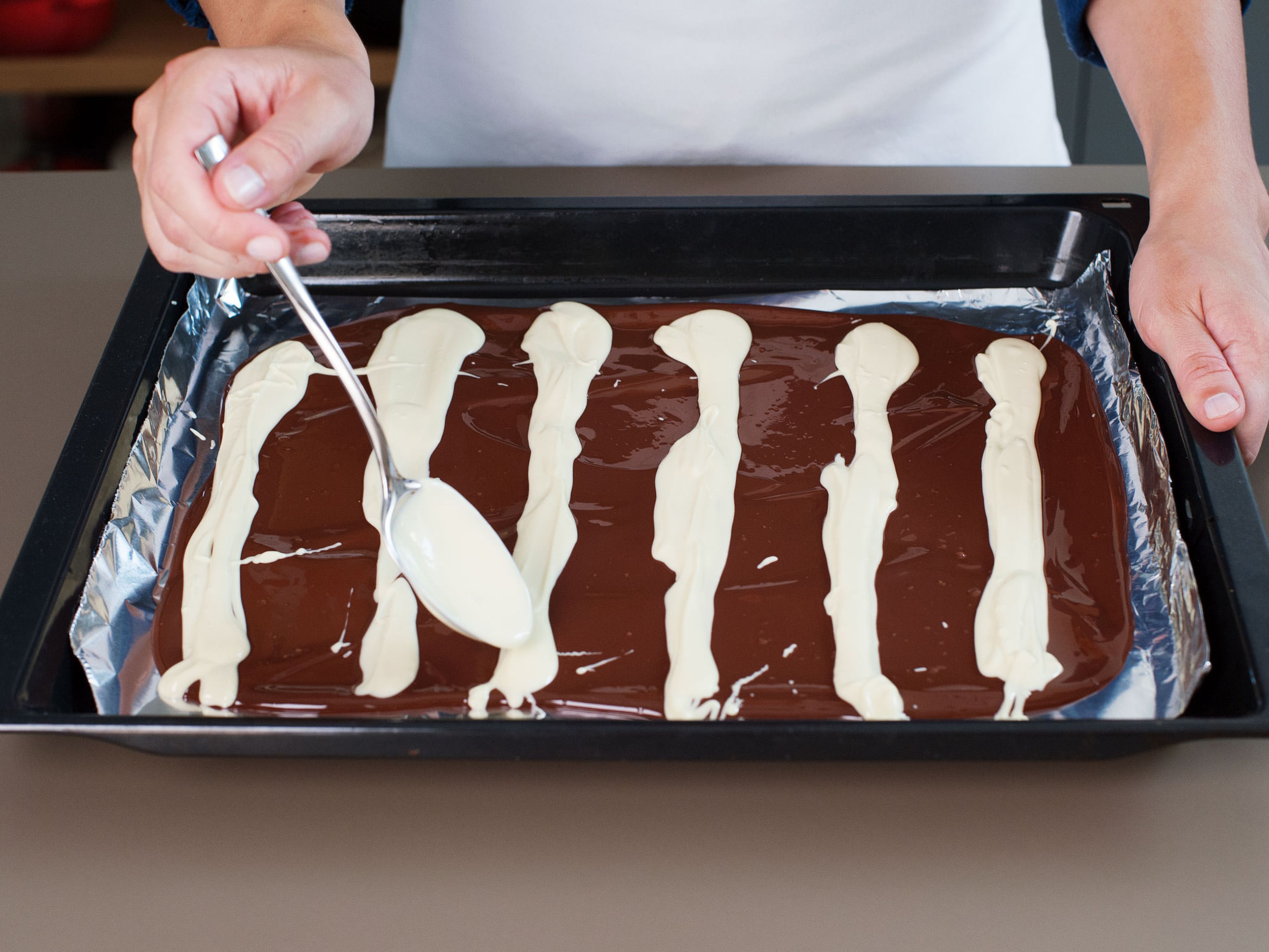 Weiße Schokolade mit einem Löffel in horizontalen Streifen mit 1 cm Abstand auf die Zartbitterschokolade geben.