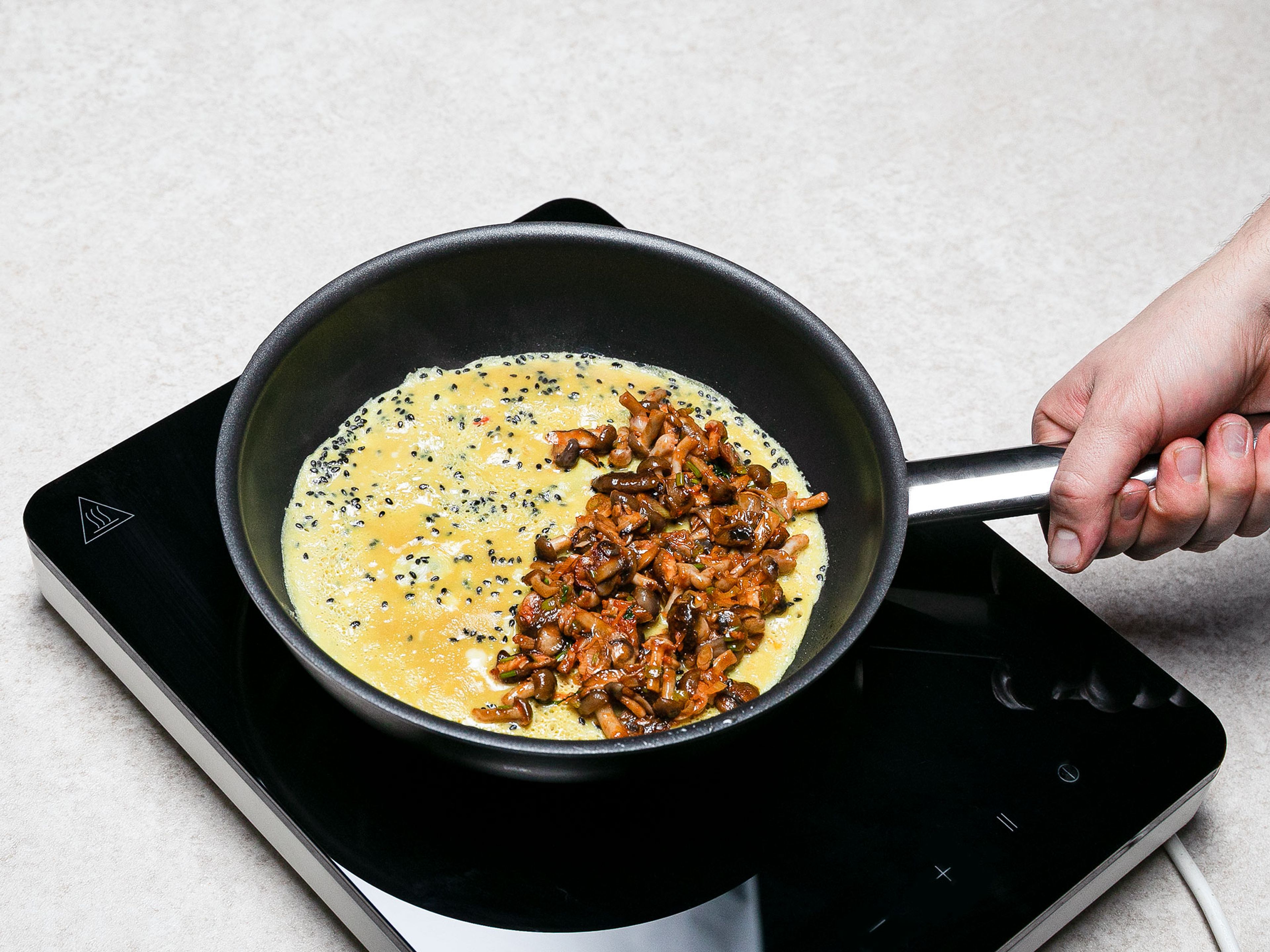 Pflanzenöl in einer großen Pfanne erhitzen. Eier mit Fischsauce, schwarzen Sesam und Chili in einer Rührschüssel verquirlen. Mit Salz und Pfeffer abschmecken. Hälfte der Eier in die heiße Pfanne geben und zu einem dünnen Crêpe ausbacken. Danach die Hälfte der zubereiteten Pilzmischung auf eine Seite geben und zu einem Omelette zusammenfalten. Mit den restlichen Zutaten wiederholen, um ein zweites Omelette zuzubereiten.