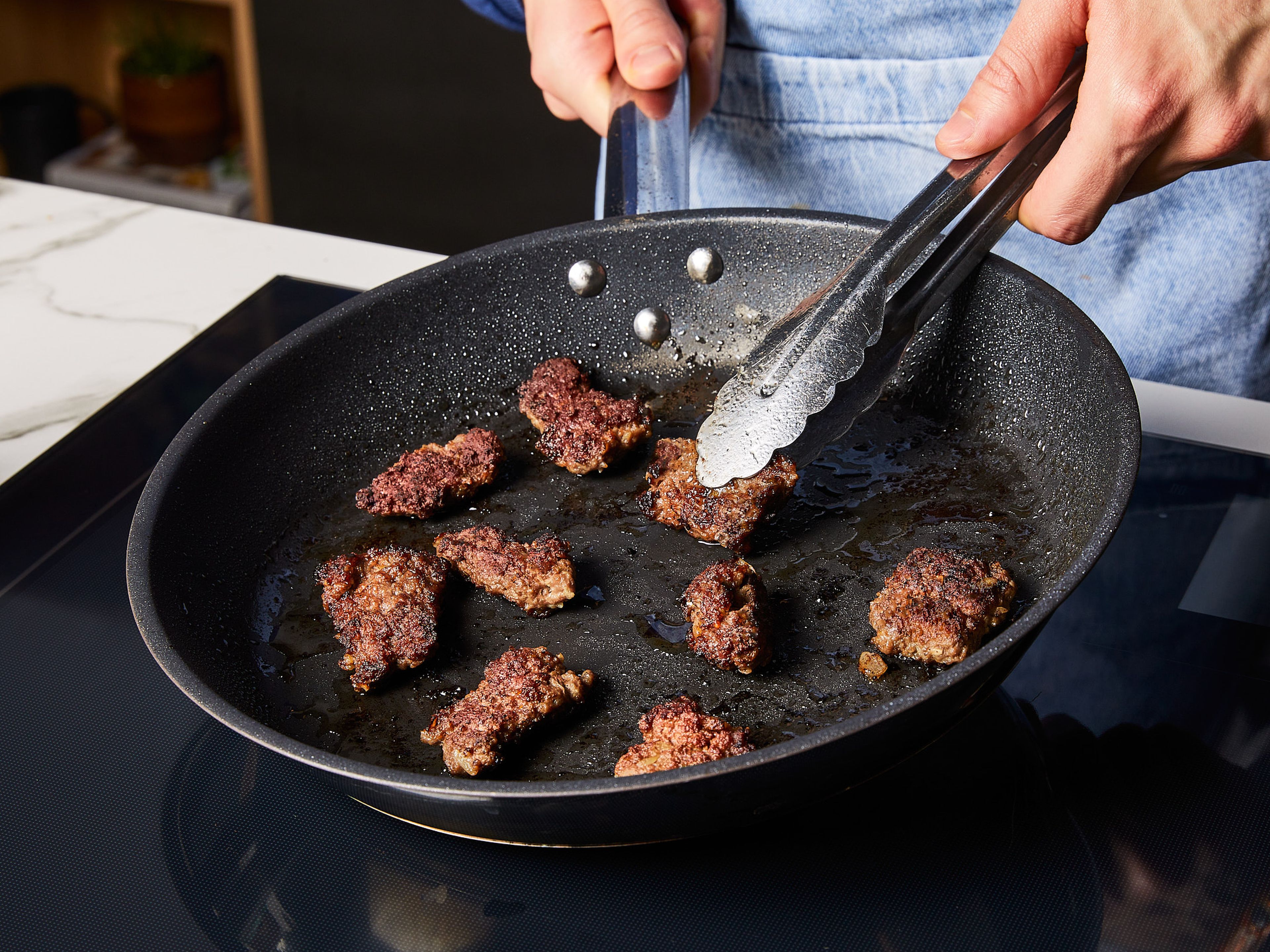 Etwas Öl in einer Pfanne erhitzen. Die Köfte-Stücke vorsichtig in die heiße Pfanne legen und darauf achten, dass sie mit Öl bedeckt sind. Alle paar Sekunden wenden, bis sie goldbraun sind. Währenddessen die Burger-Brötchen halbieren und bei 180°C Umluft ca. 5 Min. im Ofen aufwärmen. Sie sollen nur warm, aber nicht zu knusprig werden. Den Knoblauch reiben. In einer Schüssel Joghurt mit der Hälfte des Knoblauchs für die Basis-Sauce vermengen. In einem kleinen Topf Butter schmelzen, Tomatenmark, Paprikapulver, Chiliflocken und die andere Hälfte Knoblauch dazugeben und verrühren, bis alles gut vermischt ist.