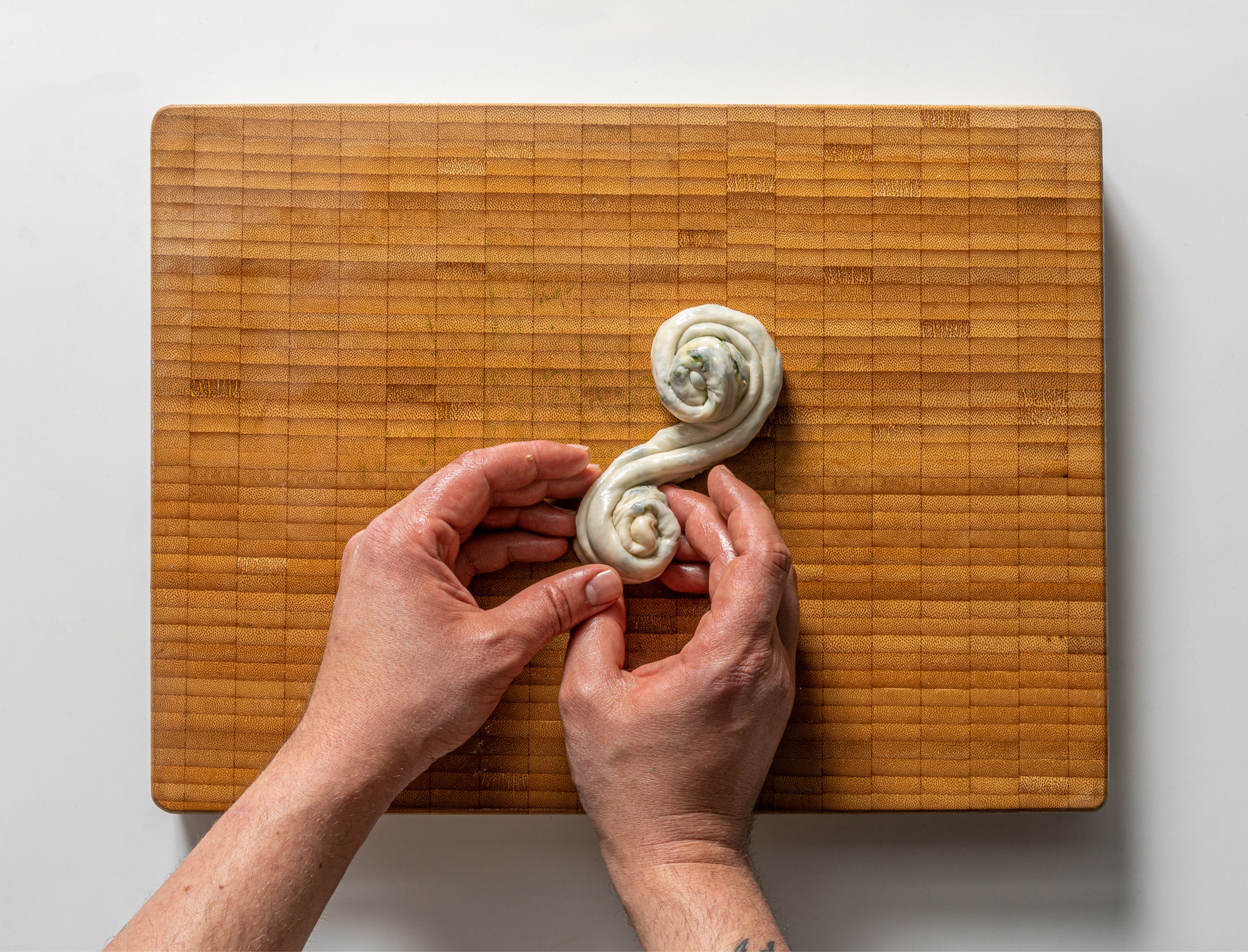 After the dough has rested, grease a large wooden cutting board. Divide the dough into equal pieces. Roll out into a rectangle until very thin using an oiled rolling pin. Spread some of the wild garlic filling on top. Roll up into a long thin snake and stretch both sides out by pulling gently. Roll the log from both sides into a snail and set aside to rest; if you’re making a large batch, brush a thin layer of oil while they rest so they don’t dry out. Repeat with the rest of the ingredients. Flatten each disk with a rolling pin again, until you have pancakes about 7 - 8 in. / 20-cm in diameter.