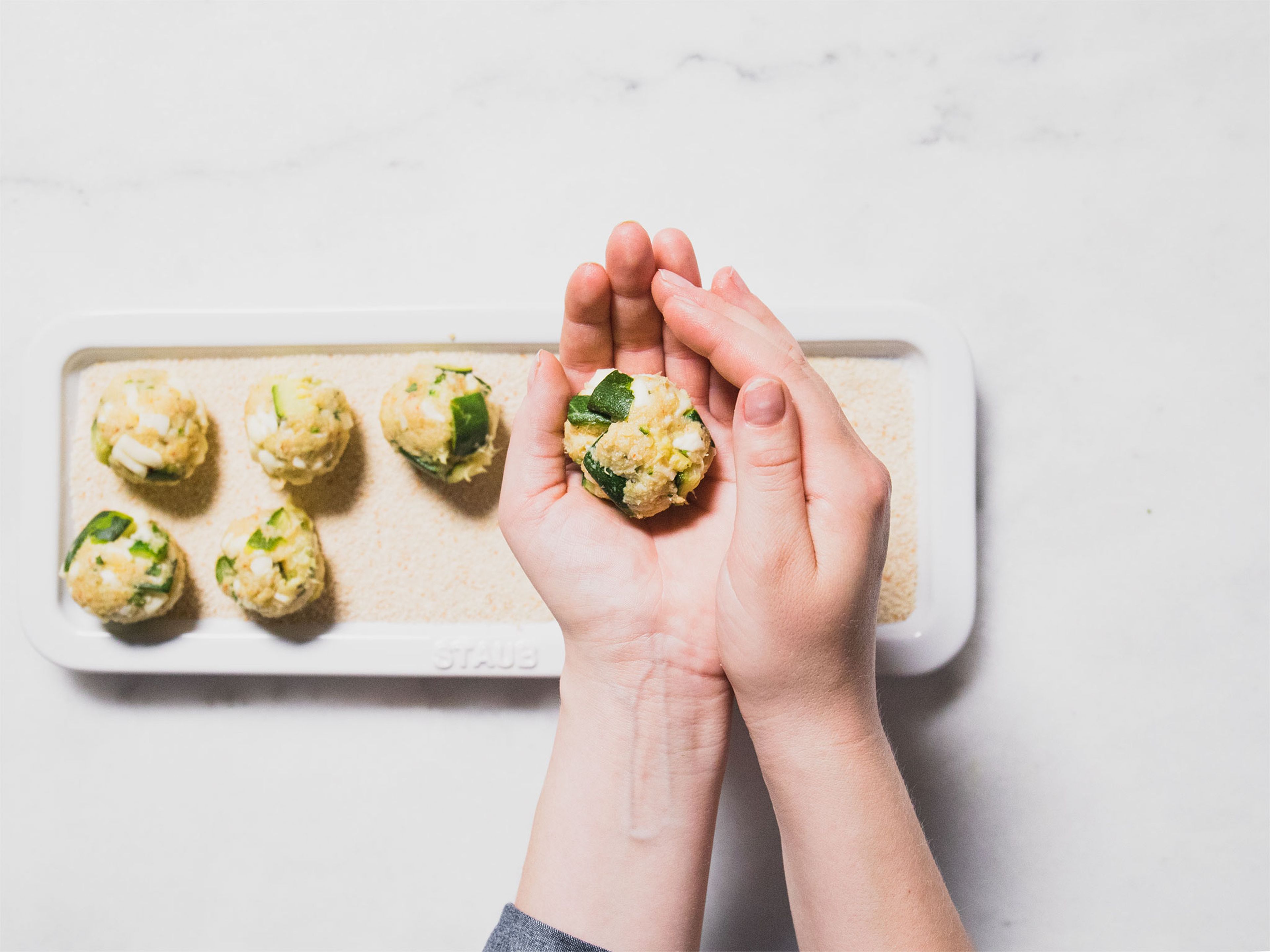Transfer zucchini mixture to a bowl and crush with a fork. Add marjoram, mozzarella, Parmesan, half the breadcrumbs, egg, Piment d'Espelette, salt, and pepper. Mix to combine. Using your hands, shape the mixture into small balls. Roll them in remaining breadcrumbs.