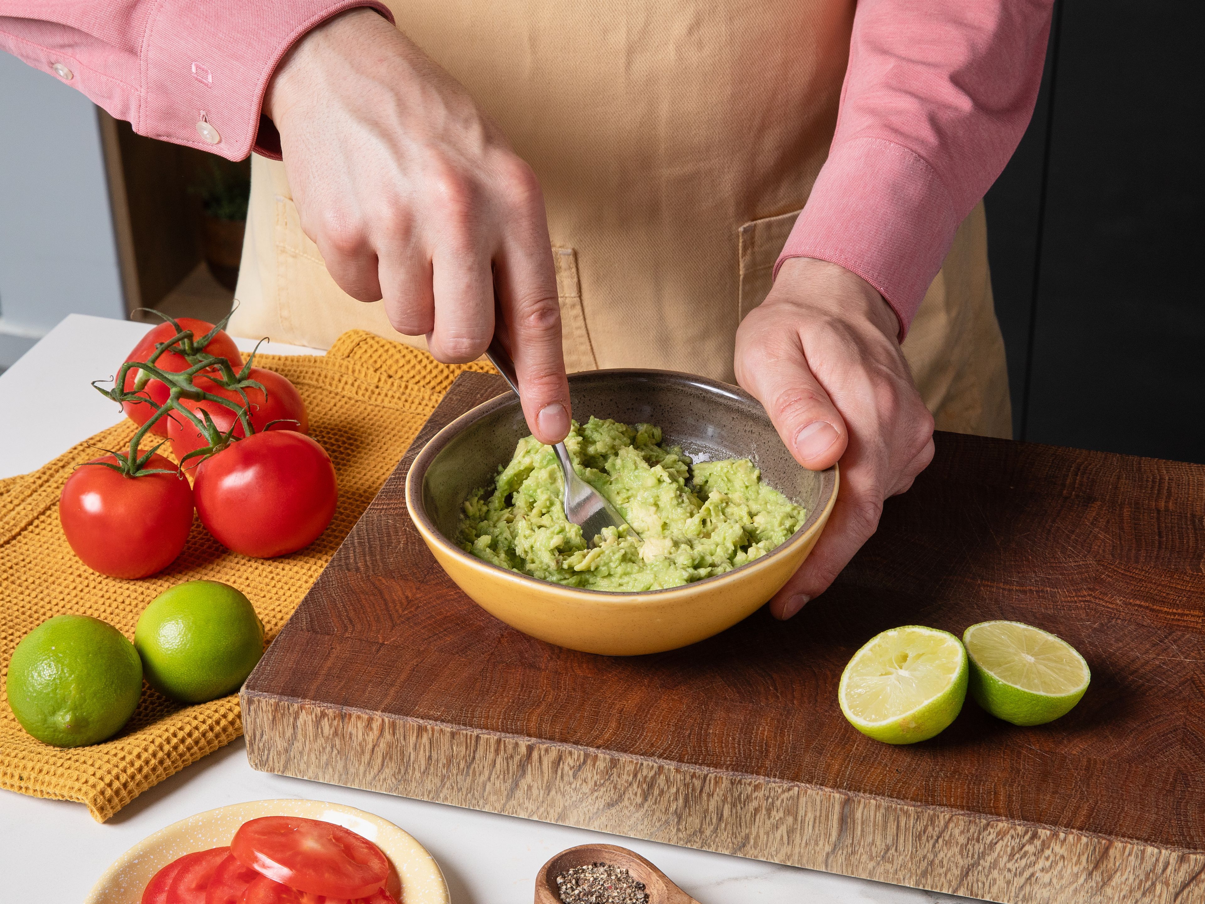Während die Eier backen, die Avocado halbieren, entkernen, das Fruchtfleisch herauslösen und mit einer Gabel zerdrücken. Die Limette halbieren und den Saft über die Avocado geben, alles mit Salz und Pfeffer abschmecken. Die Tomate in feine Scheiben schneiden.