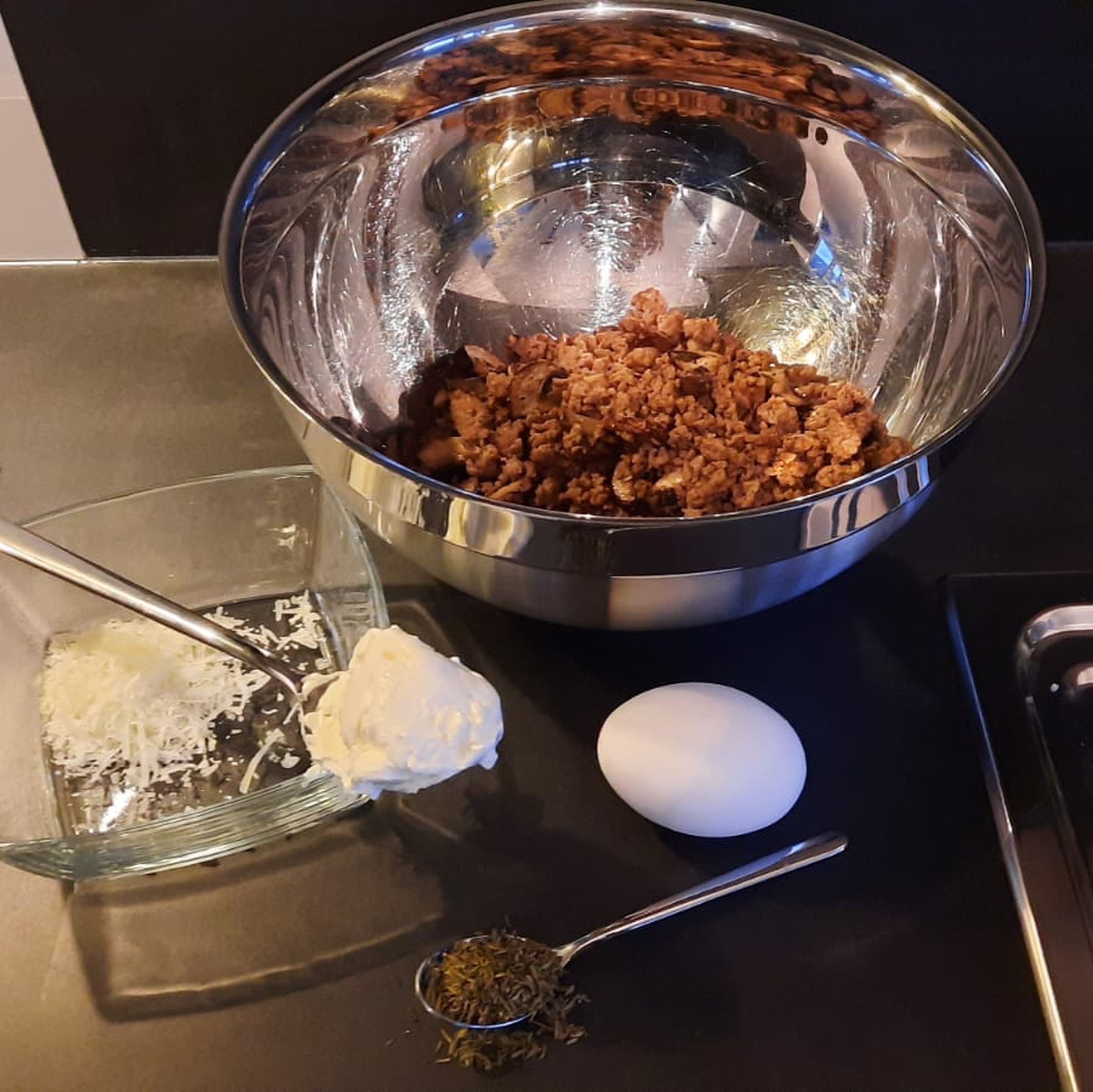 Das Hackfleisch mit den Champignons in einer Schüssel mit Schmand, Ei, gehackter Petersilie und Parmesan vermischen. Mit Salz und Pfeffer würzen.