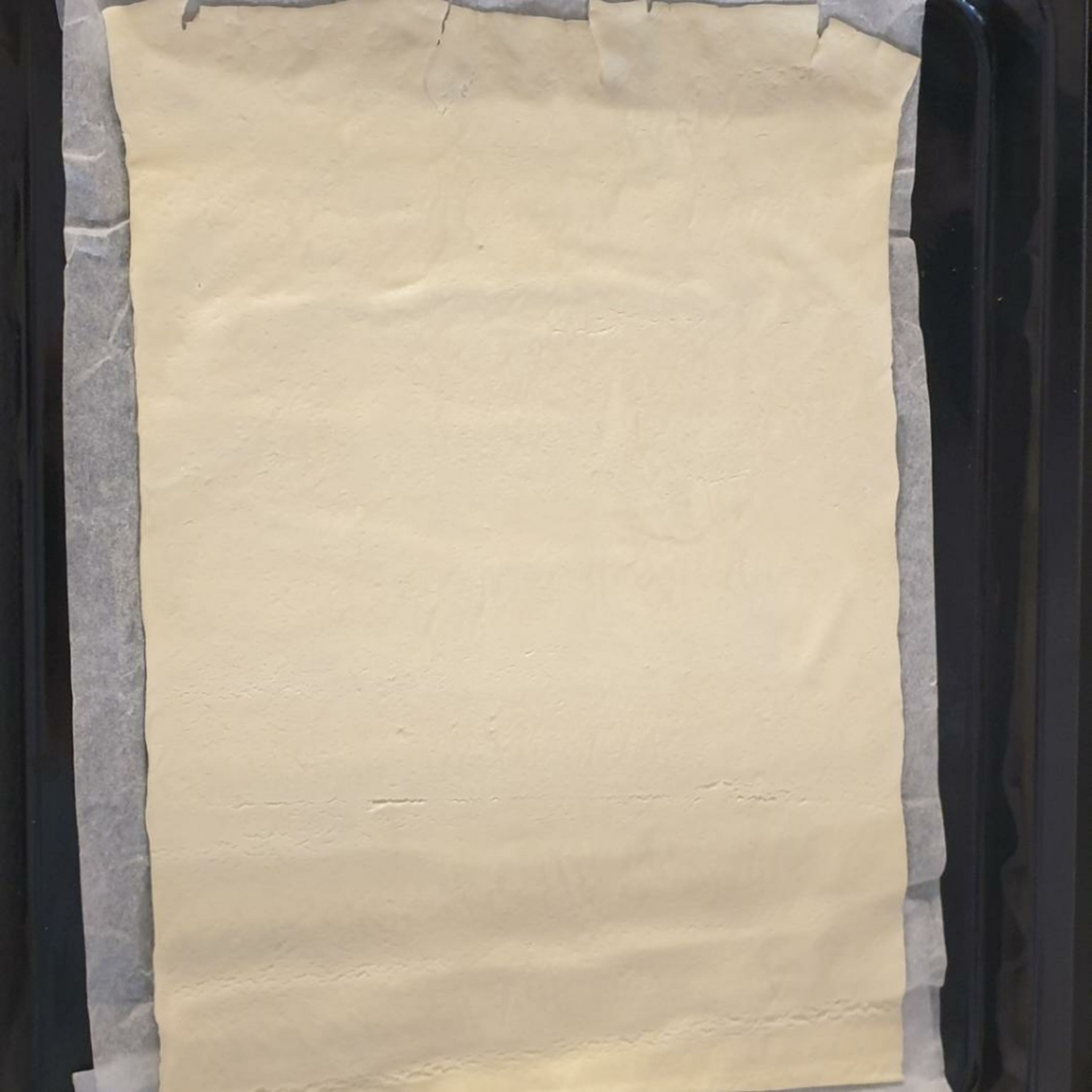 Den Flammkuchenteig aus der Verpackung nehmen und auf einem Blech ausrollen.