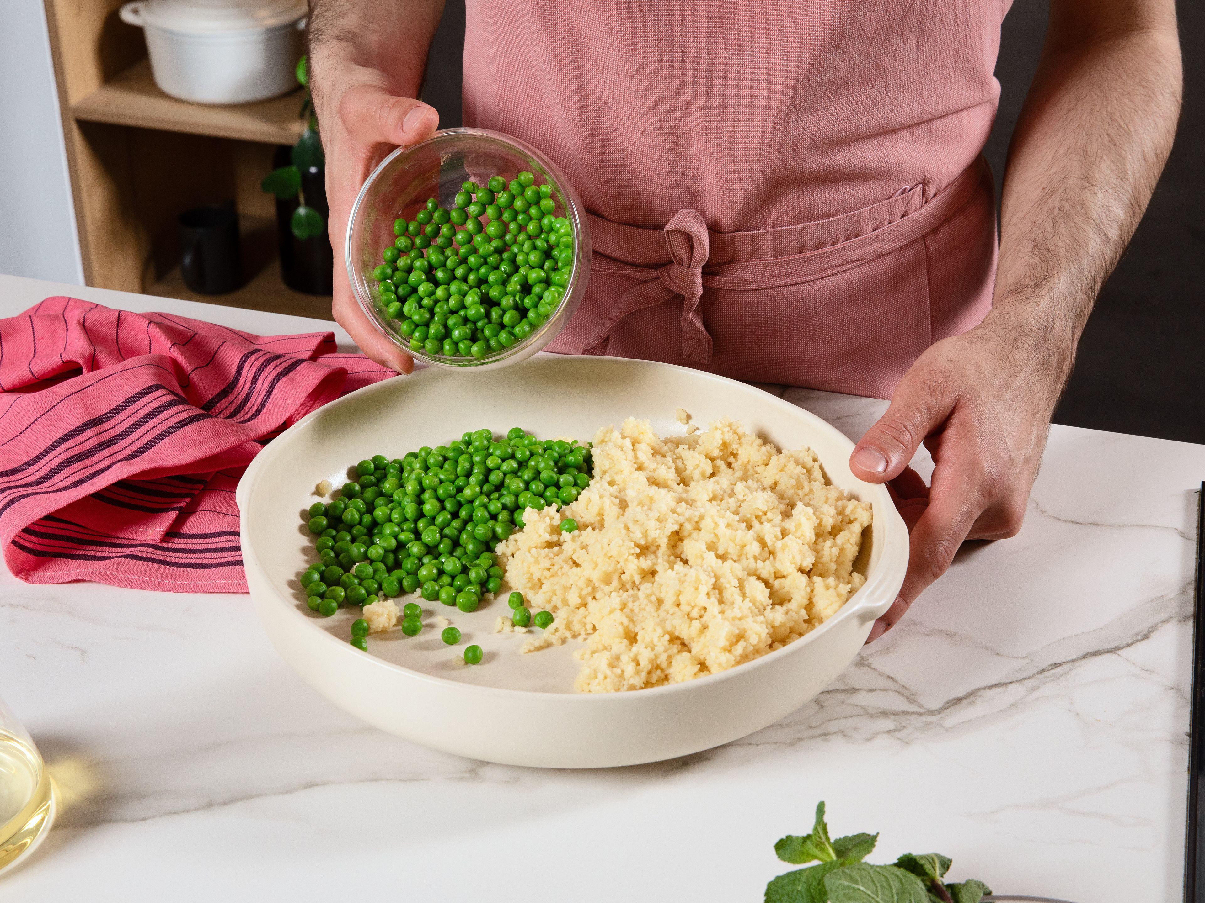 In einer Schüssel Couscous mit heißem Wasser vermengen und ca. 10–15 Min. quellen lassen. Anschließend mit einer Gabel auflockern und auf eine große Servierplatte geben. Währenddessen die Erbsen ca. 5 Min. in heißem Wasser auftauen und ebenfalls dazugeben.