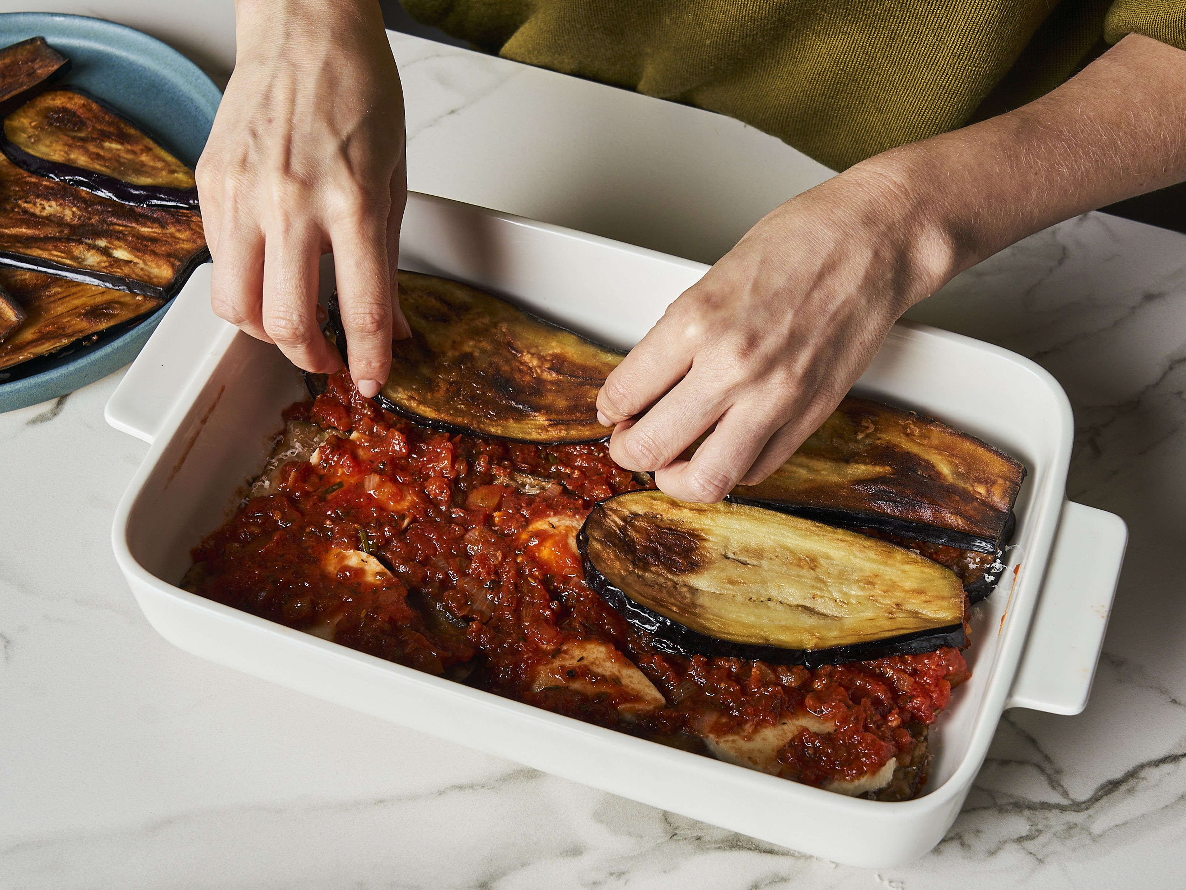 Den Backofen auf 180°C vorheizen. In einer Auflaufform Schichten mit folgender Reihenfolge erstellen: Tomatensoße, Auberginen, Mozzarella und etwas Parmesan darüber reiben. Ca. 1–2 Mal wiederholen, je nach Größe der Auflaufform.