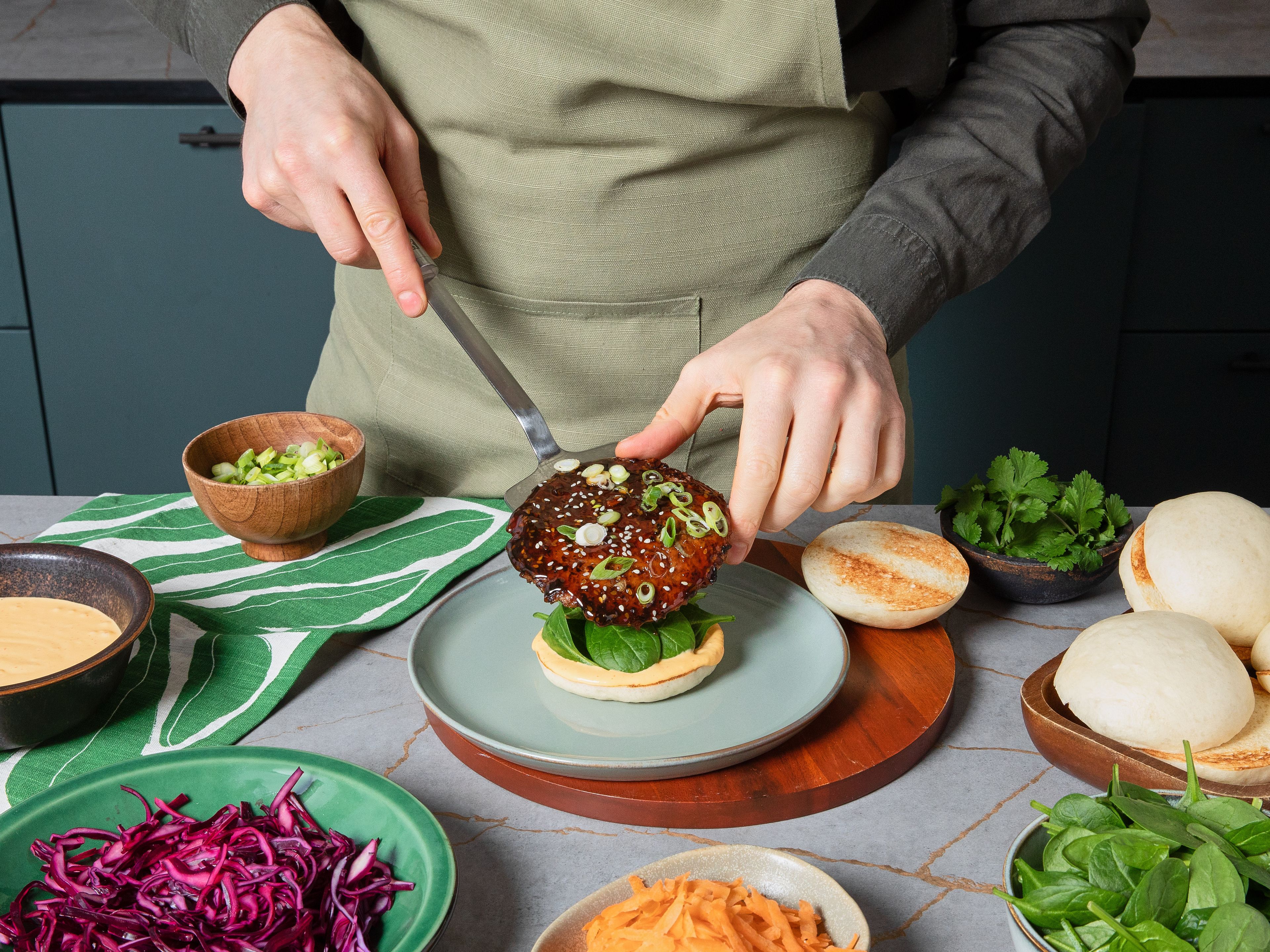 Die Unterseiten der Reis-Buns mit der veganen Mango-Mayonnaise bestreichen, Babyspinat darauf verteilen, jeweils 2 glasierte Garden Gourmet Sensational Burger darauf setzen und mit Rotkohl, Karotte und frischem Koriander toppen, anschließend mit den Bun-Deckeln schließen. Die Burger sofort servieren und die warmgehaltenen Edamame salzen und als Beilage dazu reichen.