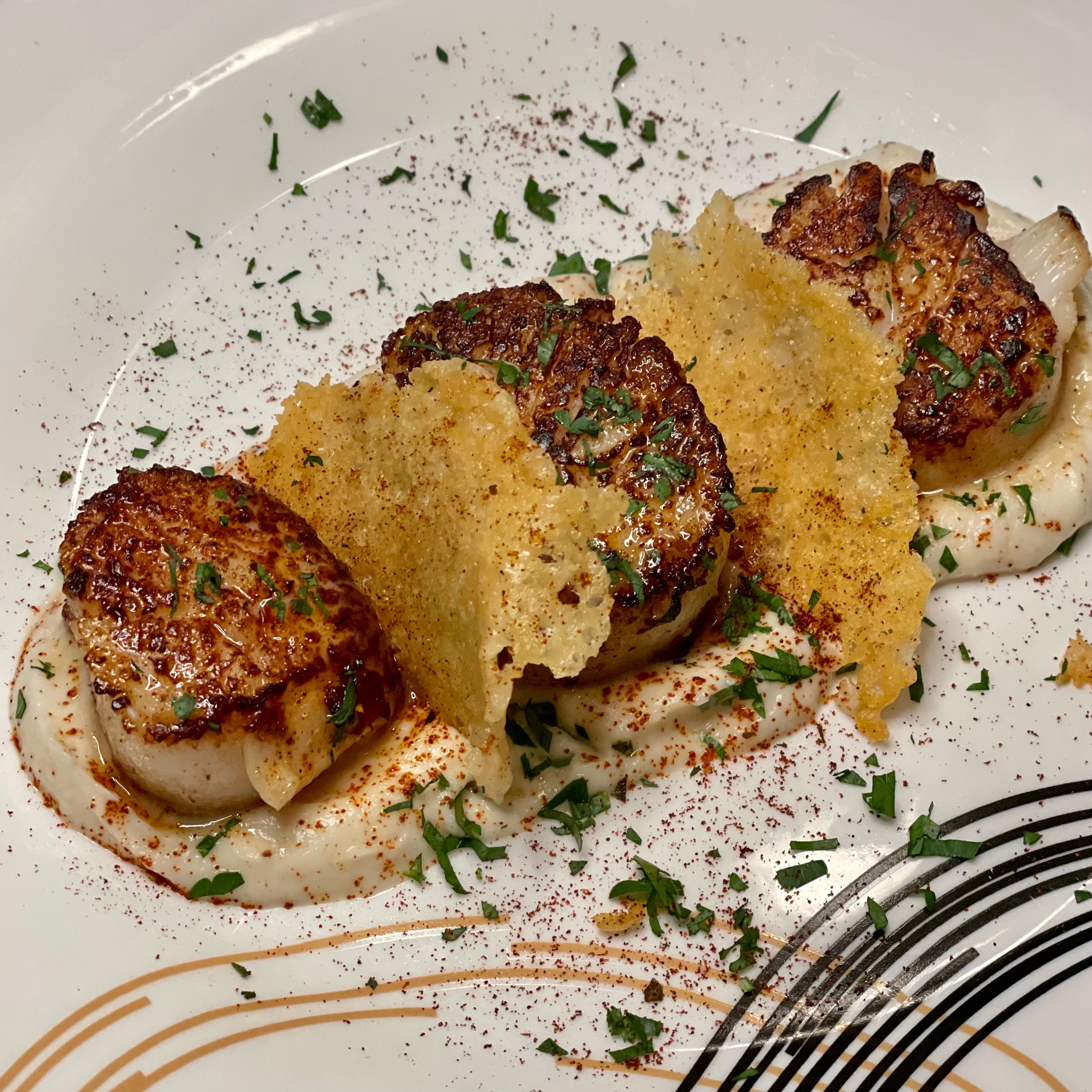 Plate cauliflower cream then put scallops on top. Finish with chopped parsley or another herb and a parmesan frico, made by putting grated parm in a pan until in browns and hardens. Sprinkle some paprika or sumac for color. 

