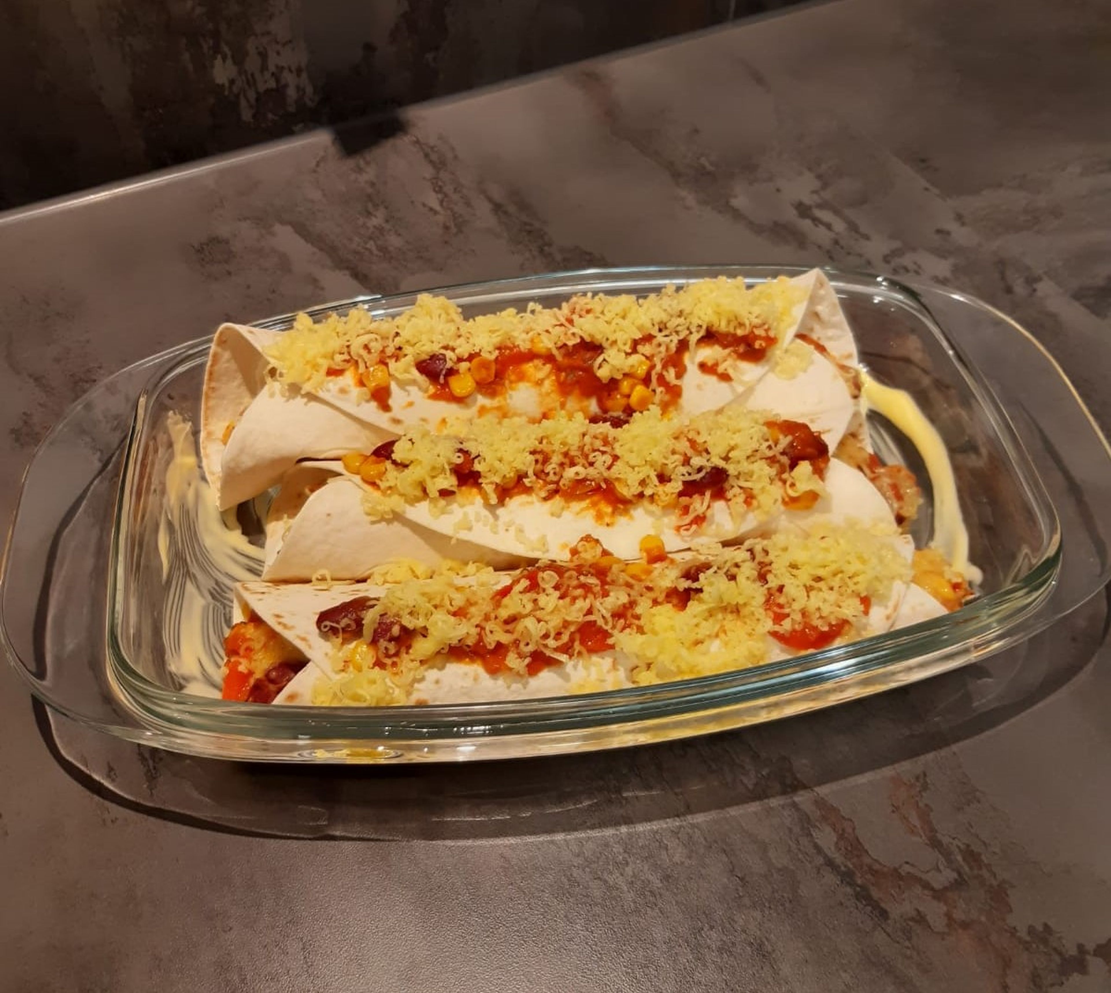 Die Tortillas aufrollen und in eine eingefettete Auflaufform legen. Tortillas gleichmäßig mit Tomatensoße bestreichen und mit restlichem Käse bestreuen.