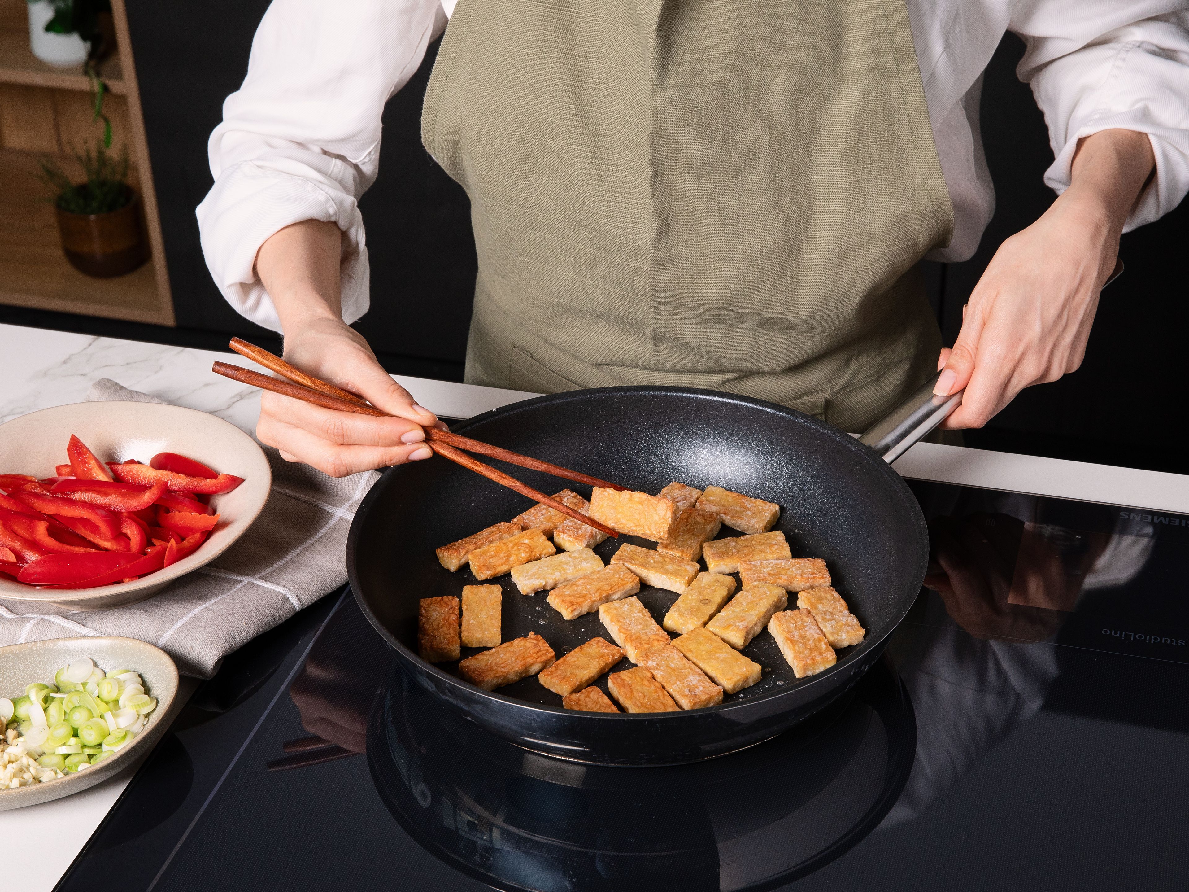 Speiseöl in einer großen Pfanne oder einem Wok erhitzen. Tempeh darin ca. 5 Min. von allen Seiten goldbraun braten, herausnehmen und beiseitestellen. Im restlichen Öl Brokkolini, Paprika, Frühlingszwiebelweiß, Knoblauch und Ingwer ca. 3–4 Min. anbraten.