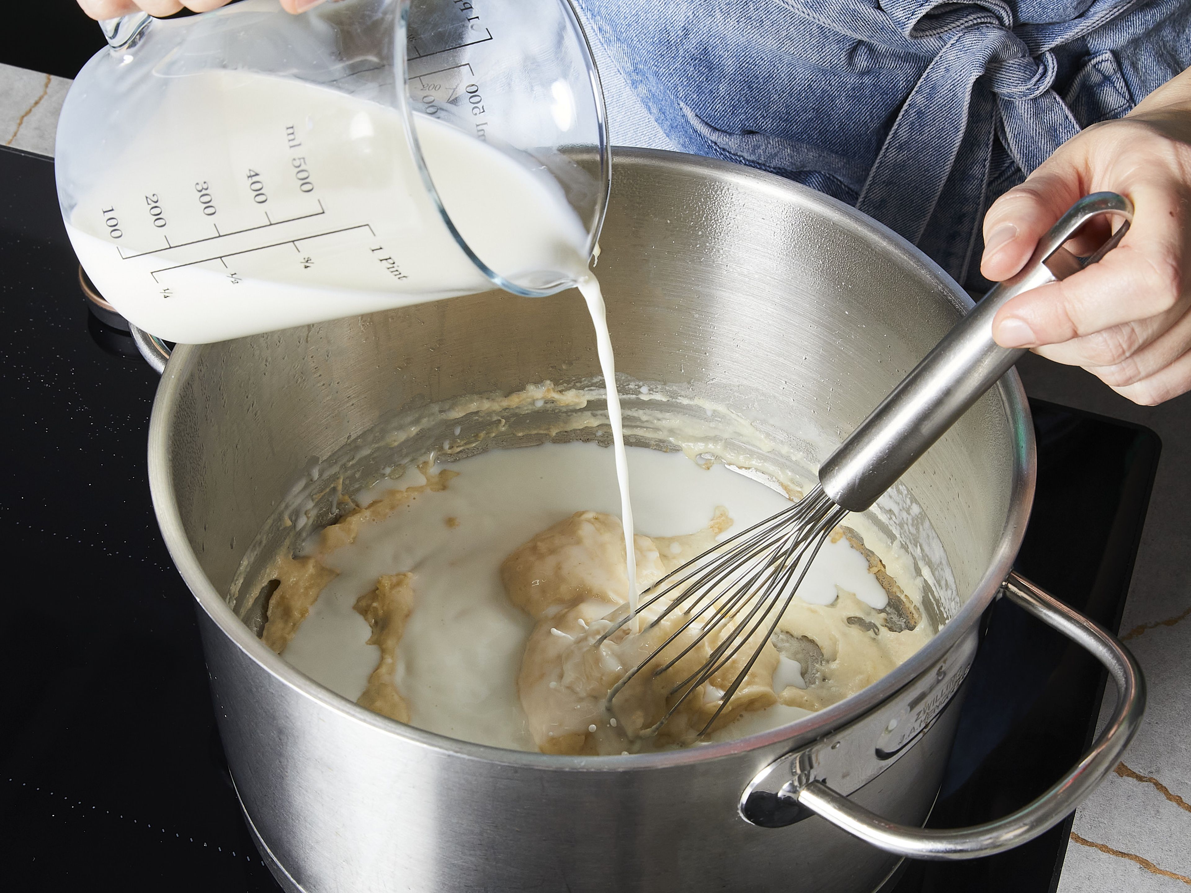 Den Cheddar-Käse mit einer Küchenmaschine oder Reibe zerkleinern und beiseitestellen. In einem großen Topf bei mittlerer Hitze die Butter zerlassen. Das Mehl einrühren und unter ständigem Rühren ca. 2 Min. kochen, bis die Mischung eingedickt ist und eine leicht goldene Farbe angenommen hat. Etwas Milch dazugeben und weiterrühren. Sobald die Mischung eingedickt ist, die restliche Milch und das Wasser hinzufügen und zum Kochen bringen.