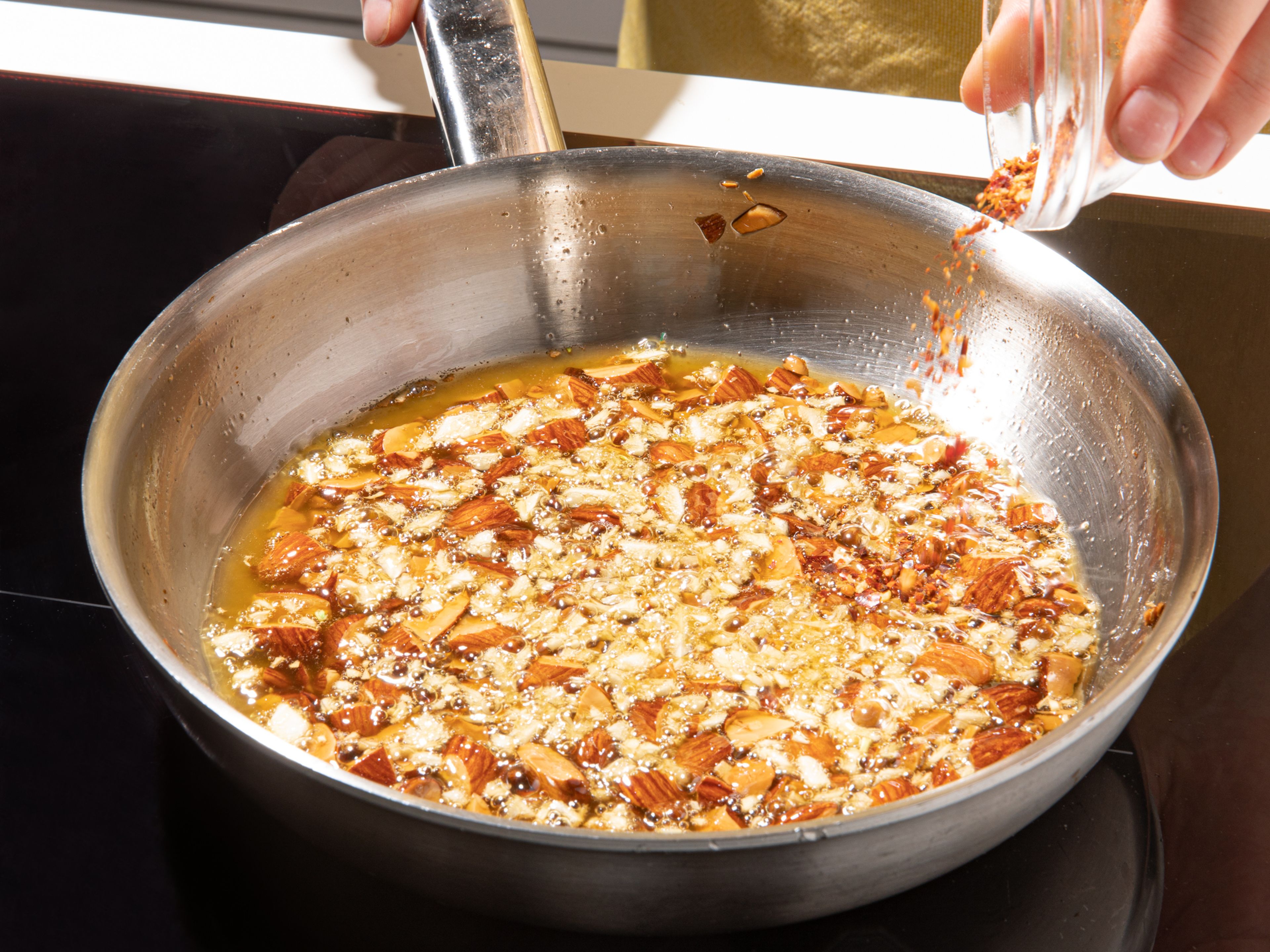 In a frying pan, heat olive oil over medium-high heat. Add almonds and fry until almost golden brown, then add garlic and fry briefly until fragrant and just about to brown. Remove from heat, then mix in cumin and chili flakes. Add salt and pepper, let cool.
