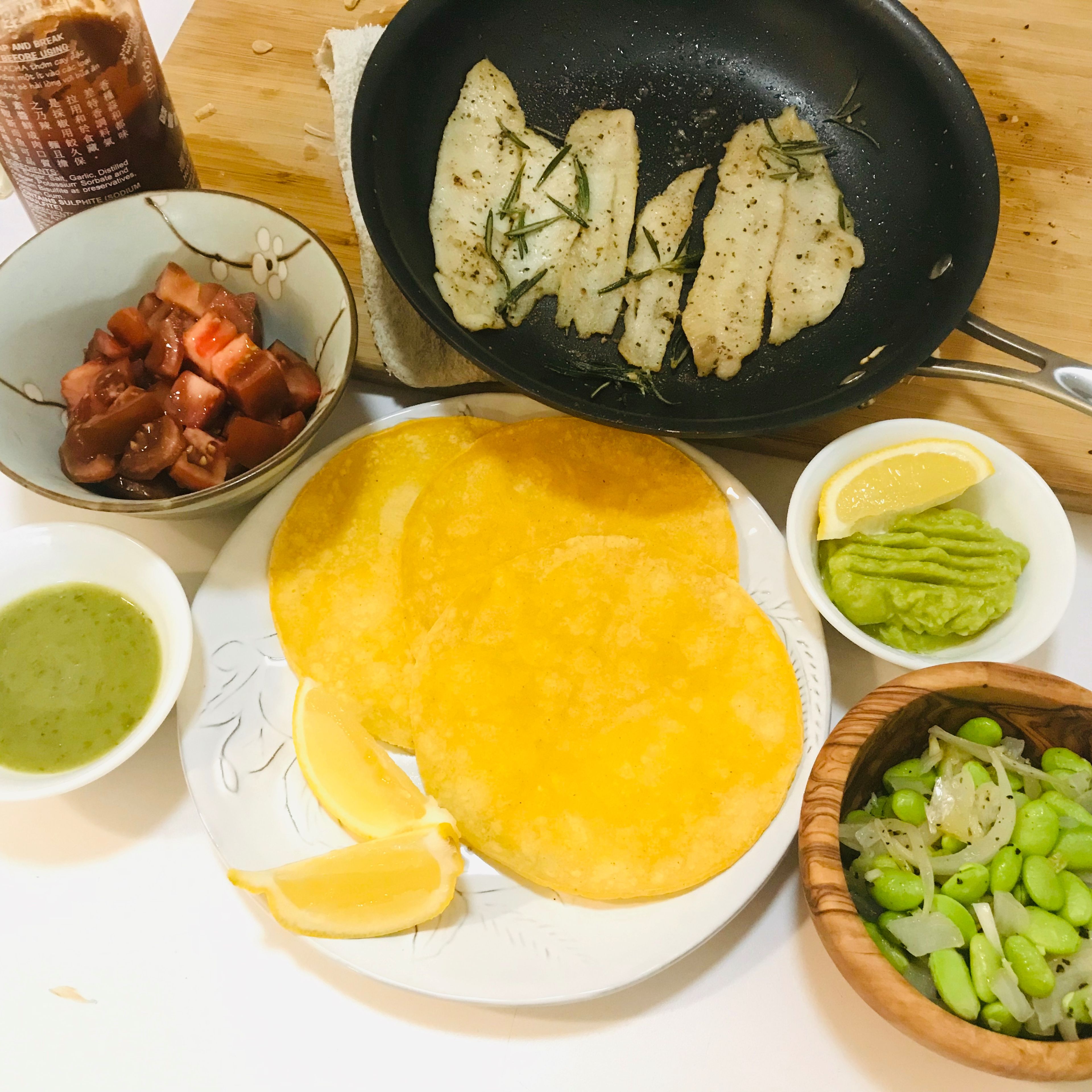 Assemble the taco! Put one piece of fish, a scoop of sautés edamame, and chopped tomatoes into a tortilla. Add a dollop of mashed avocado and drizzle some sriracha on top. Squeeze more lemon, if desired.