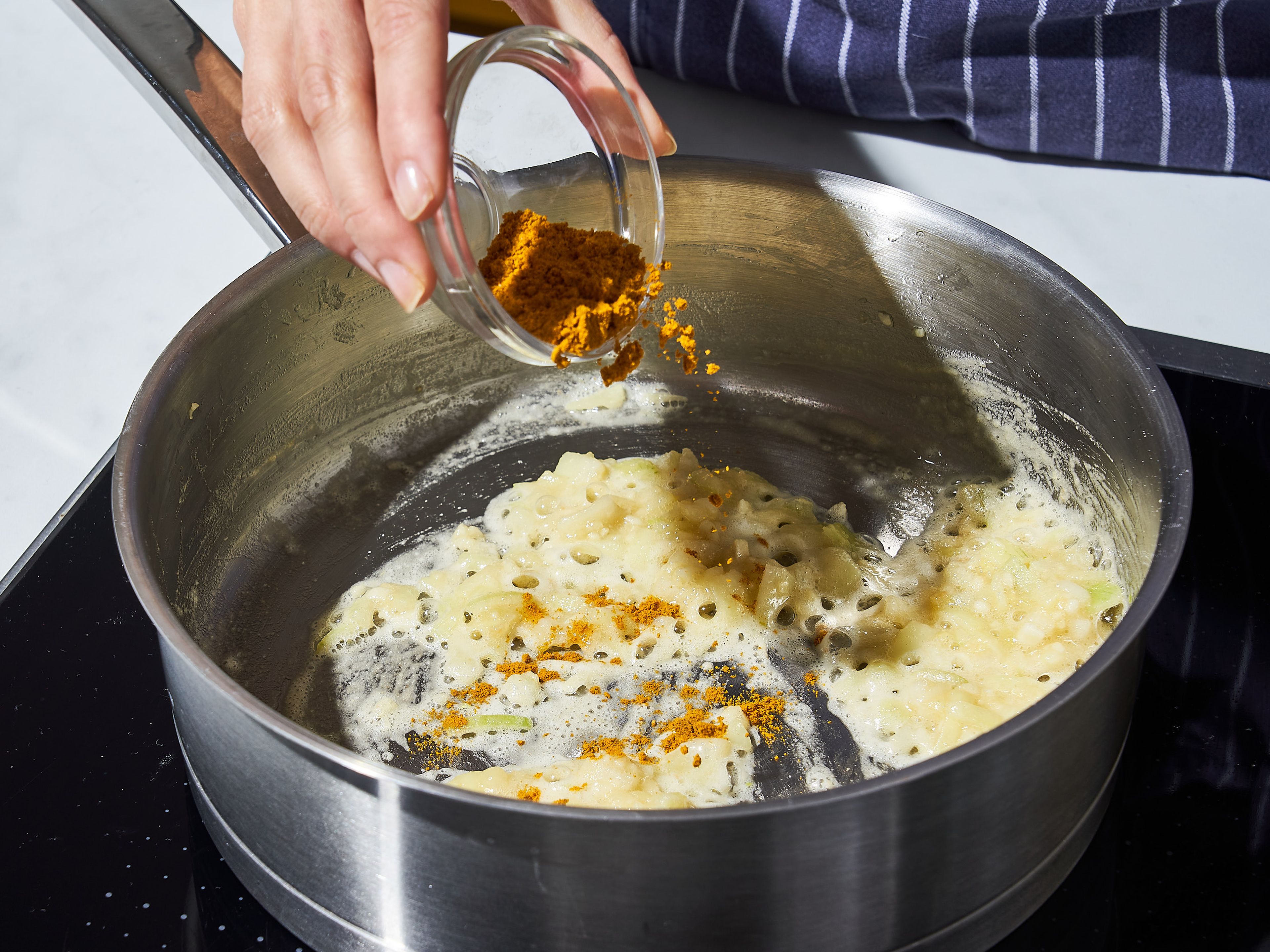 Für die Soße, Pflanzenöl in einen mittelgroßen Topf bei mittlerer Hitze geben. Gehackten Knoblauch und Zwiebeln hinzufügen und ca. 5 Min. anbraten. Butter hinzufügen und schmelzen lassen. Dann einen Teil des Mehls hinzugeben und unter ständigem Rühren ca. 4 Min. braten, bis die Mischung anfängt zu bräunen. Currypulver und bei Bedarf einige Chiliflocken einrühren und unter ständigem Rühren ca. 3 Min. weiterbraten.