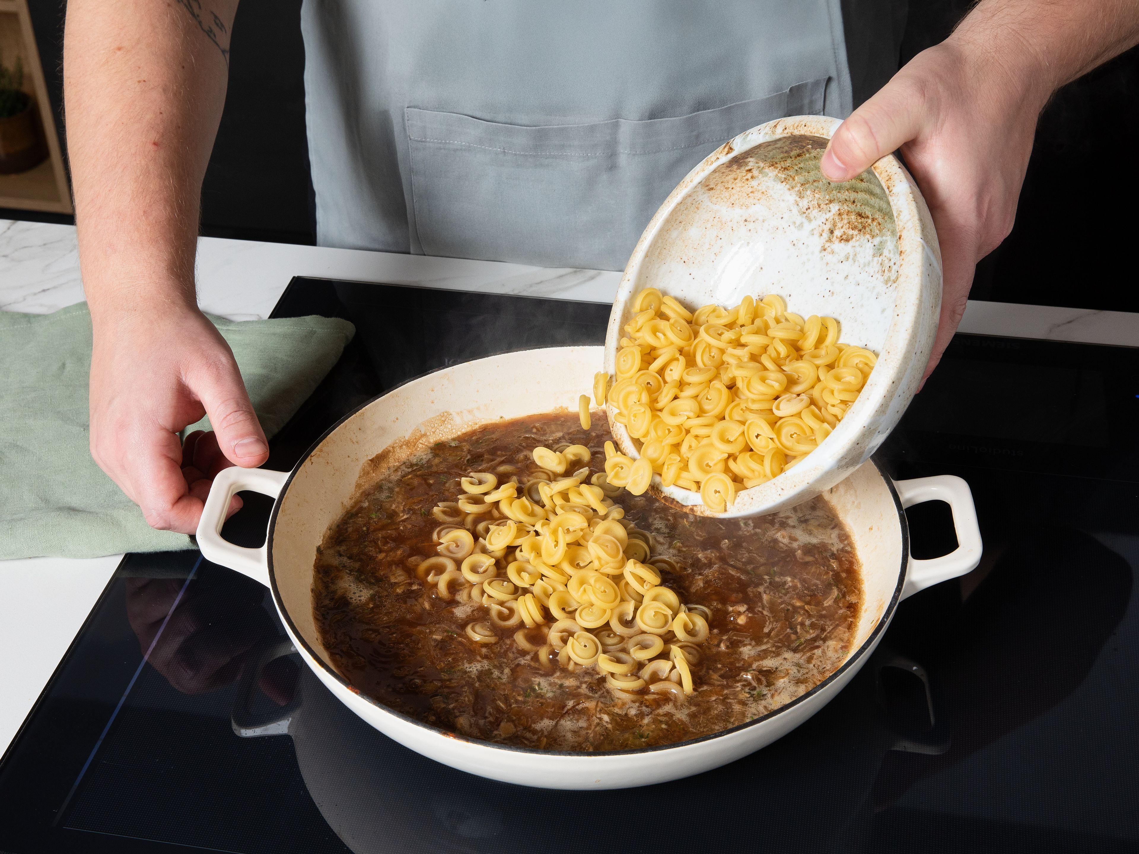 Dann die rohe Pasta und den Rinderfond in die Pfanne geben. Bei mittlerer bis hoher Hitze unter Rühren köcheln lassen, bis die Flüssigkeit aufgenommen ist und die Nudeln al dente sind. Die Thymianzweige entfernen, dann Sahne und die Hälfte des Gruyèrkäses unterrühren. Noch einmal kurz aufkochen, bis die Soße cremig ist und nach Geschmack mit Salz und Pfeffer würzen. Zum Servieren mit dem restlichen Gruyère bestreuen und nach Belieben mit frischen Thymianblättchen garnieren.
