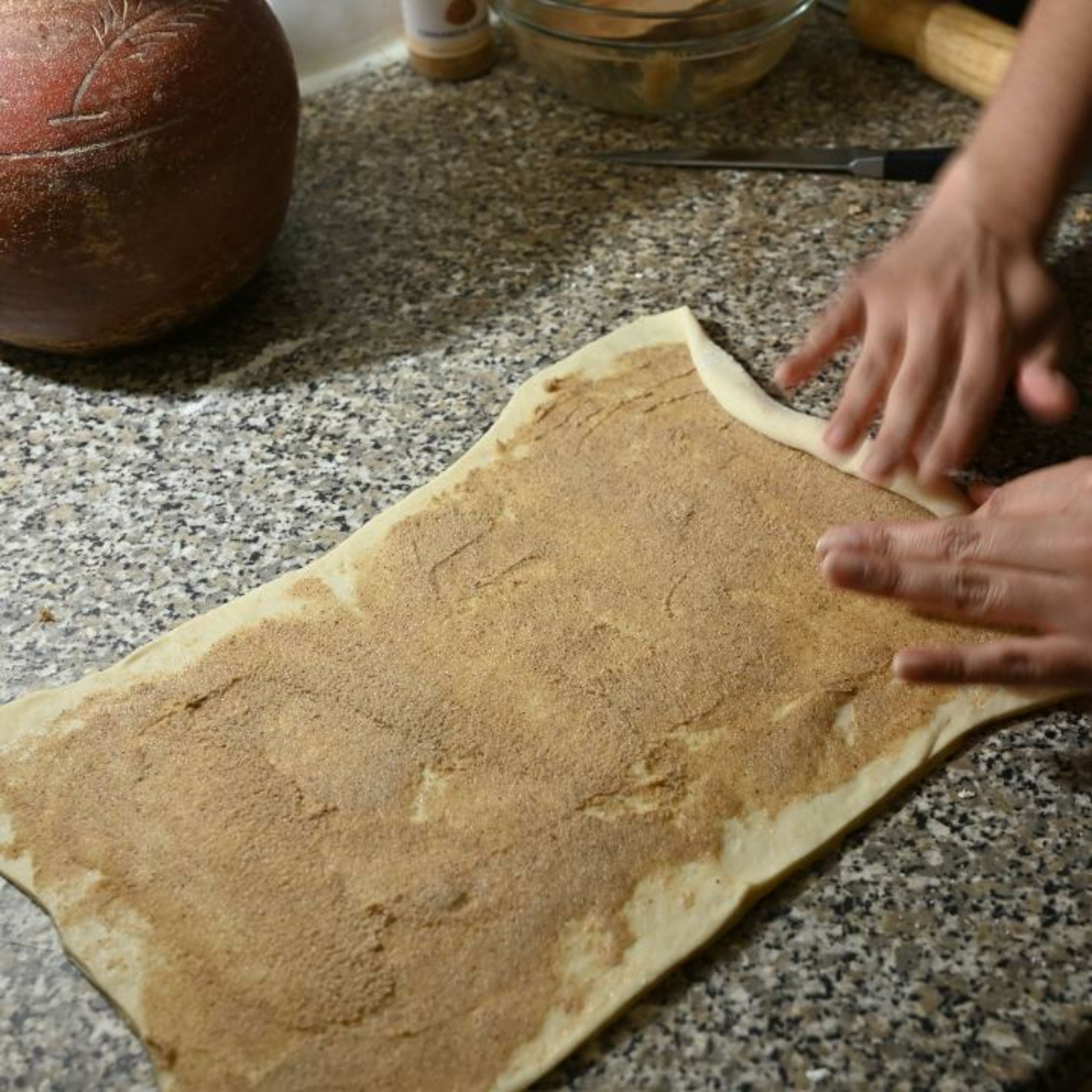 Spread the cinnamon powder and sugar mixture on to the dough. Starting from the short end, roll up the dough into a roll.