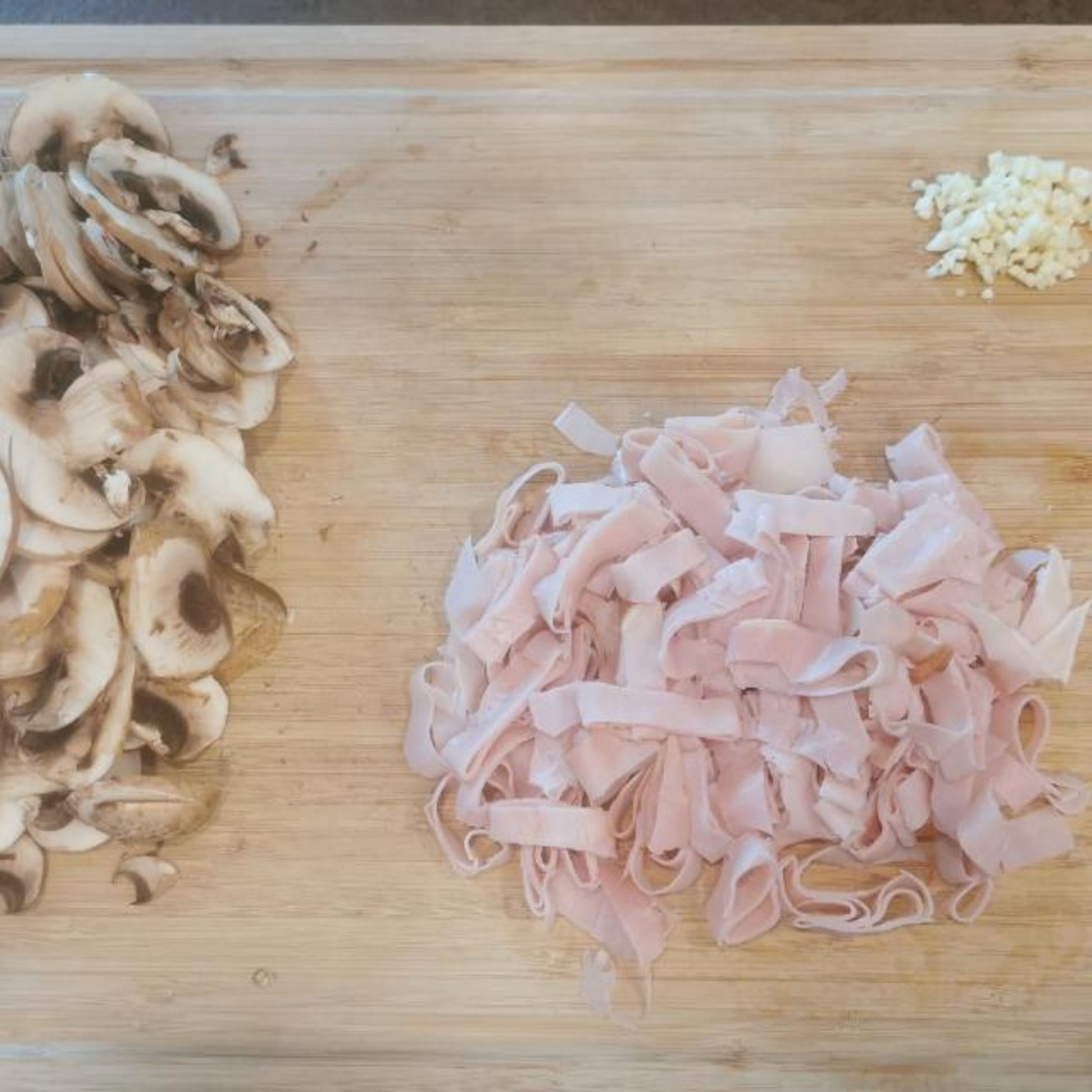 Topf mit Wasser und einer Priese Salz zum Kochen bringen. Währenddessen den Knoblauch fein hacken. Champignons putzen und in dünne Scheiben schneiden. Schinkenblätter in ca. 0,5cm breite Streifen schneiden. Zitrone auspressen und Saft beiseite stellen.