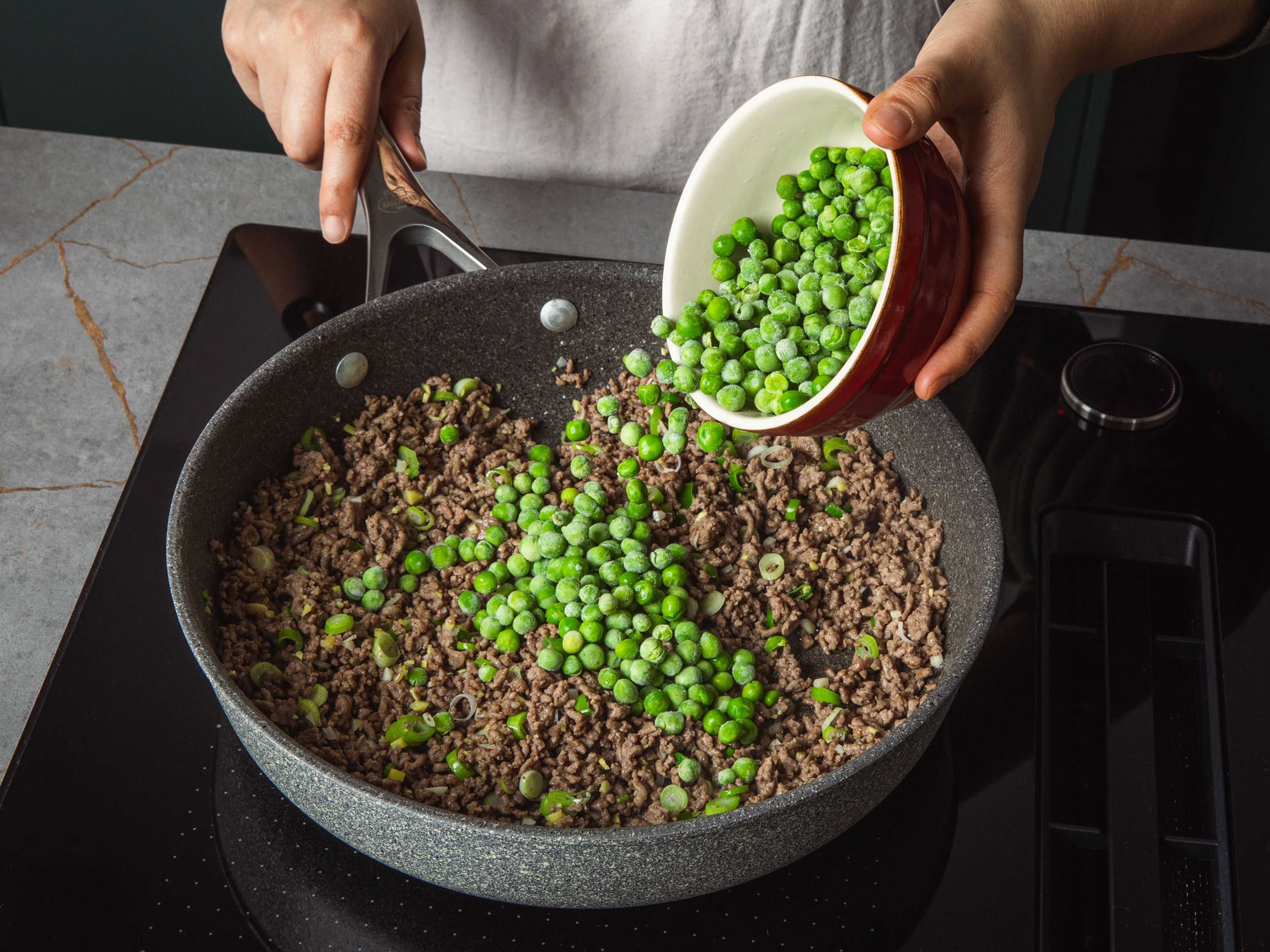 In a big frying pan, add beef mince, heat over medium heat and break it down with a spatula. Fry for approx. 7–8 min, until the meat is brown and starts to crisp up. Add scallion whites, ginger, and garlic. Stir to combine and fry for approx. 1 min. until fragrant. Then add the frozen peas and the sauce. Fry for approx. 5 min. until the sauce is reduced and the peas are cooked. Serve over the cooked rice and garnish with scallion greens.