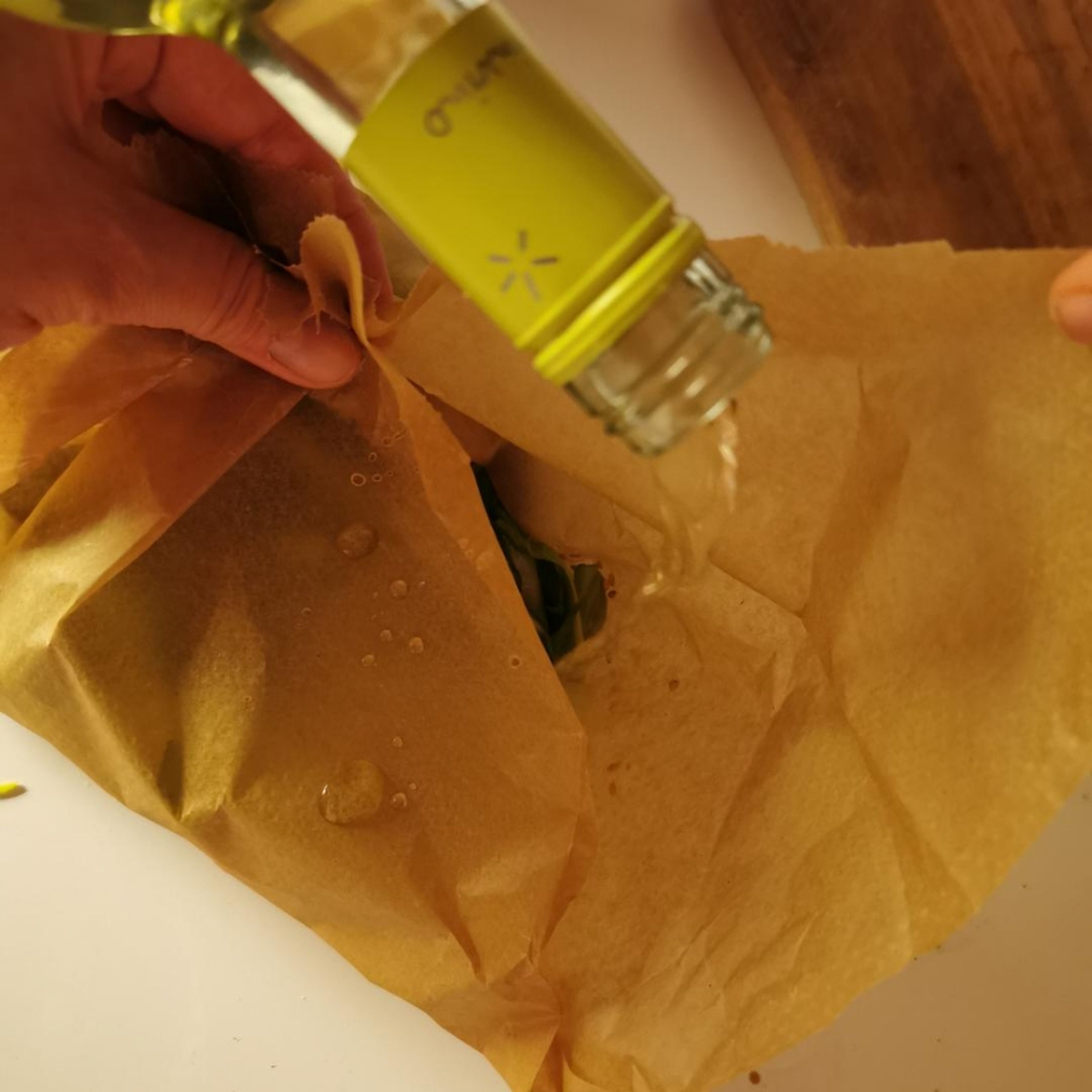 Einen Schuss Weißwein und Olivenöl in das oben zusammengefasste Backpapierbündel gießen.