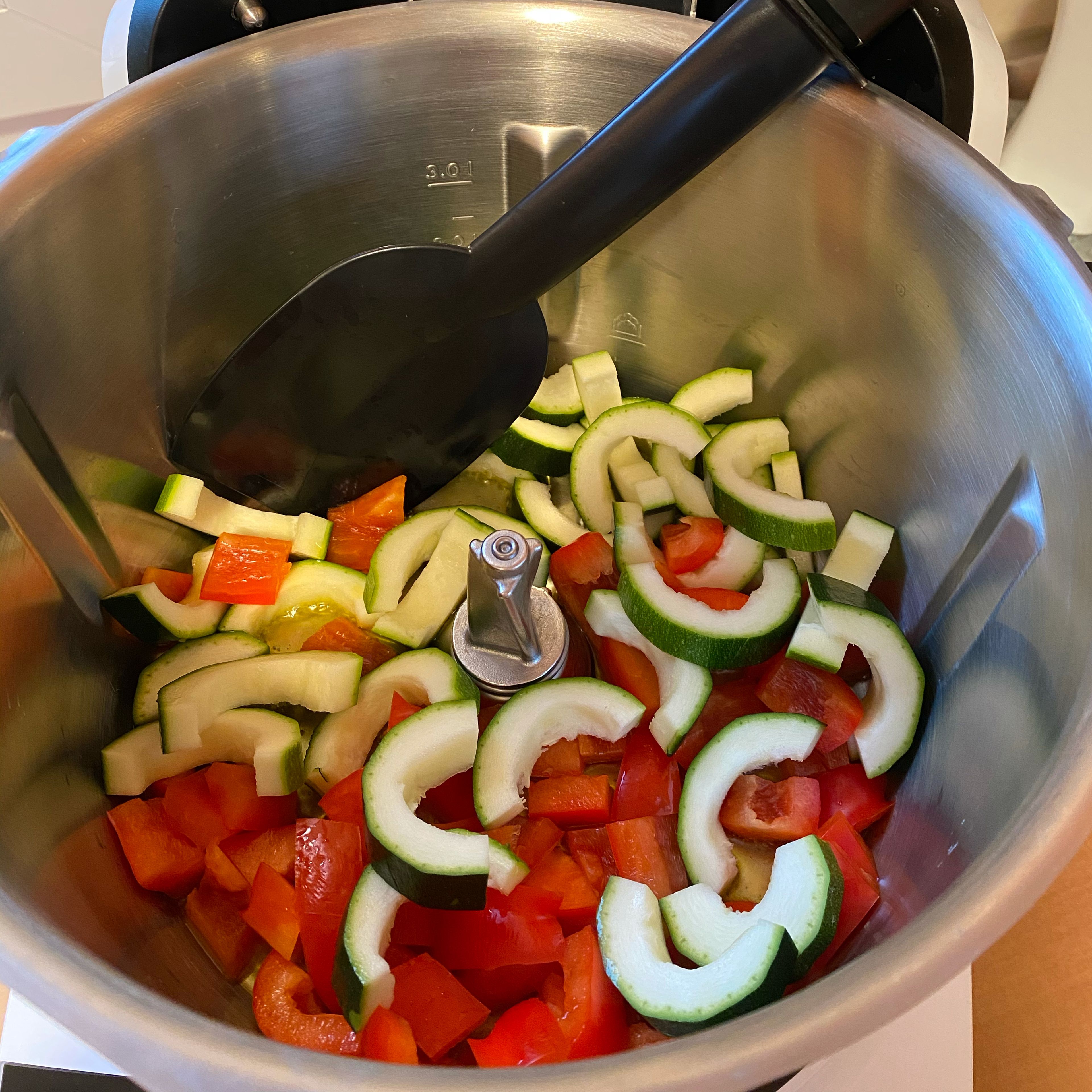 Zucchini und Paprika in den Topf geben und bei offenem Deckel  anbraten, dabei mit dem Cookit Küchenspatel gelegentlich umrühren (ohne Werkzeug | 160°C | 5 Minuten). In der letzten Minute den Knoblauch hinzugeben.