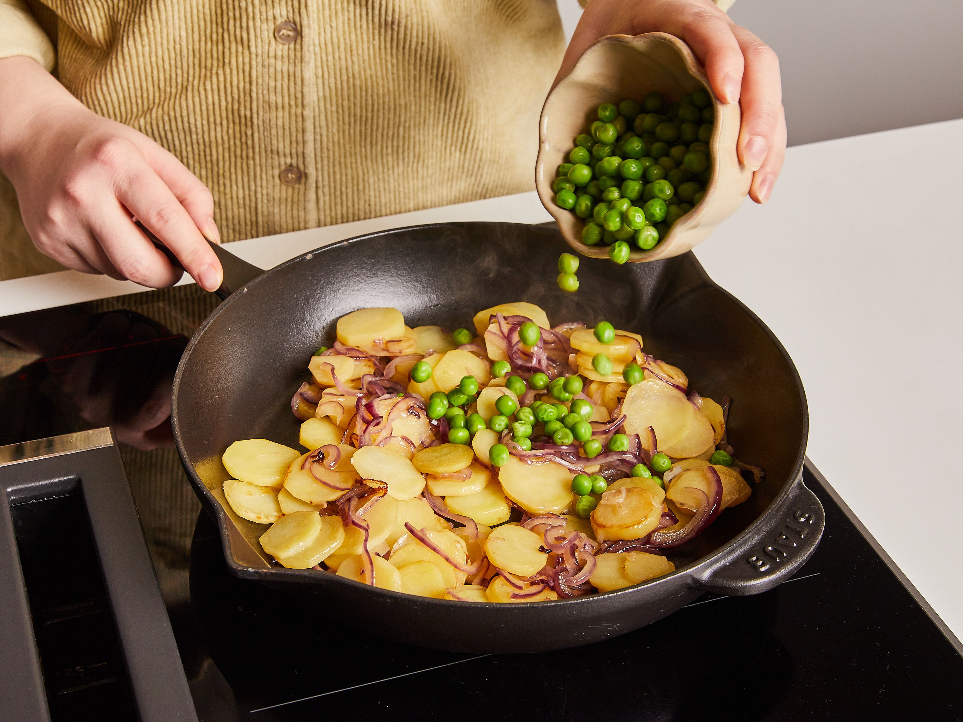 Add olive oil to a nonstick ovenproof pan, set over medium heat. Add red onion and potatoes and cook approx. 10 min., stirring often, until potatoes are fork tender. Then add peas and most of the tomatoes and continue cooking for approx. 3 min. more, or until tomatoes are softened.