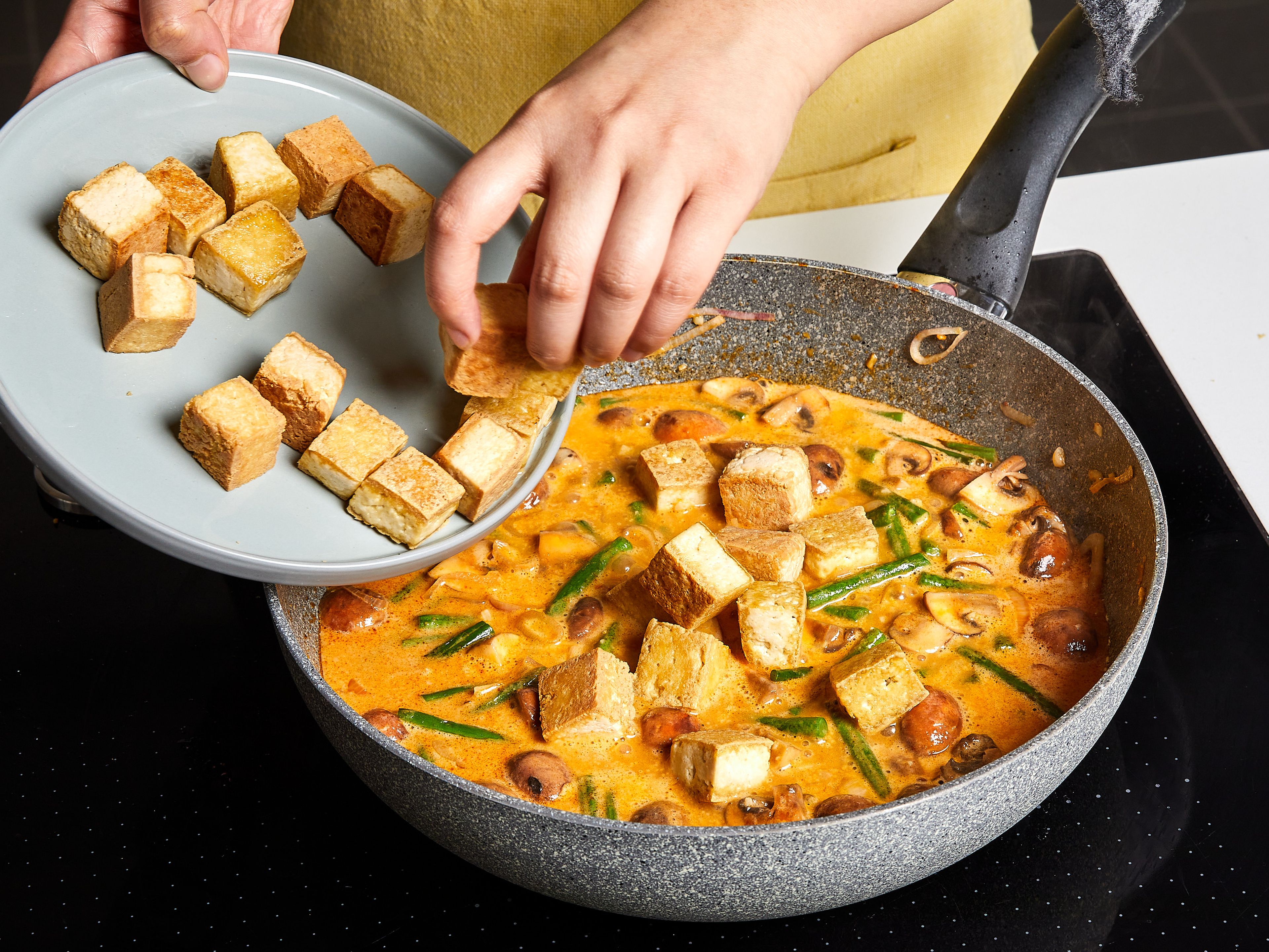 Dann Schalotten, Ingwer und Knoblauch hinzufügen und kurz anbraten, bis es duftet. Rote Currypaste dazugeben, ca. 1 Min. anbraten. Champignons dazugeben und ca. 2 Min. mitbraten. Mit Kokosmilch und Gemüsebrühe ablöschen und zum Köcheln bringen. Tofu hinzufügen und ca. 5–8 Min. köcheln lassen, bis das Curry etwas eindickt. Sojasauce und Zucker dazugeben und mit Salz abschmecken.