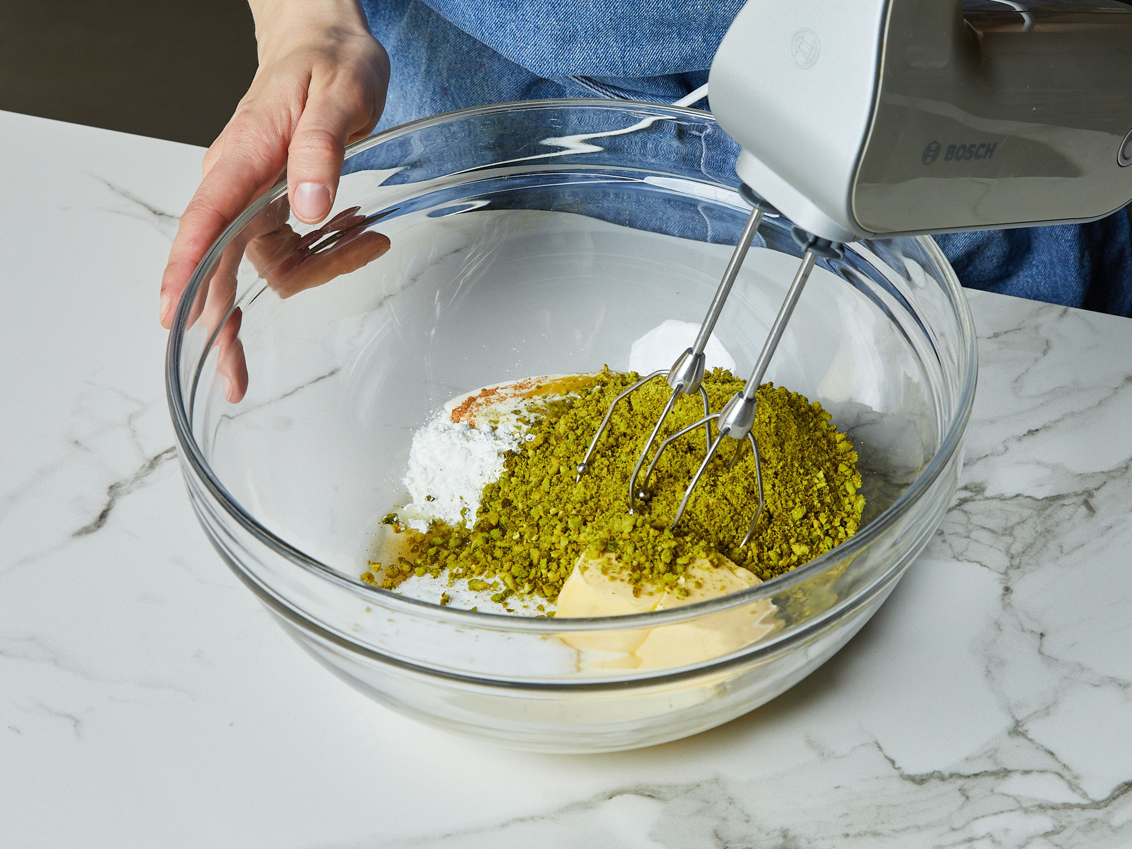 For the filling, chop most of the pistachios very finely using a knife or food processor. Coarsely chop the remaining pistachios, and set aside. Put the pistachio flour into a large bowl and whip it with starch, salt, room temperature butter, vanilla extract, eggs, heavy cream, ground cinnamon, ground cardamom, and remaining sugar for approx. 2–3 min. with a hand mixer until fluffy.