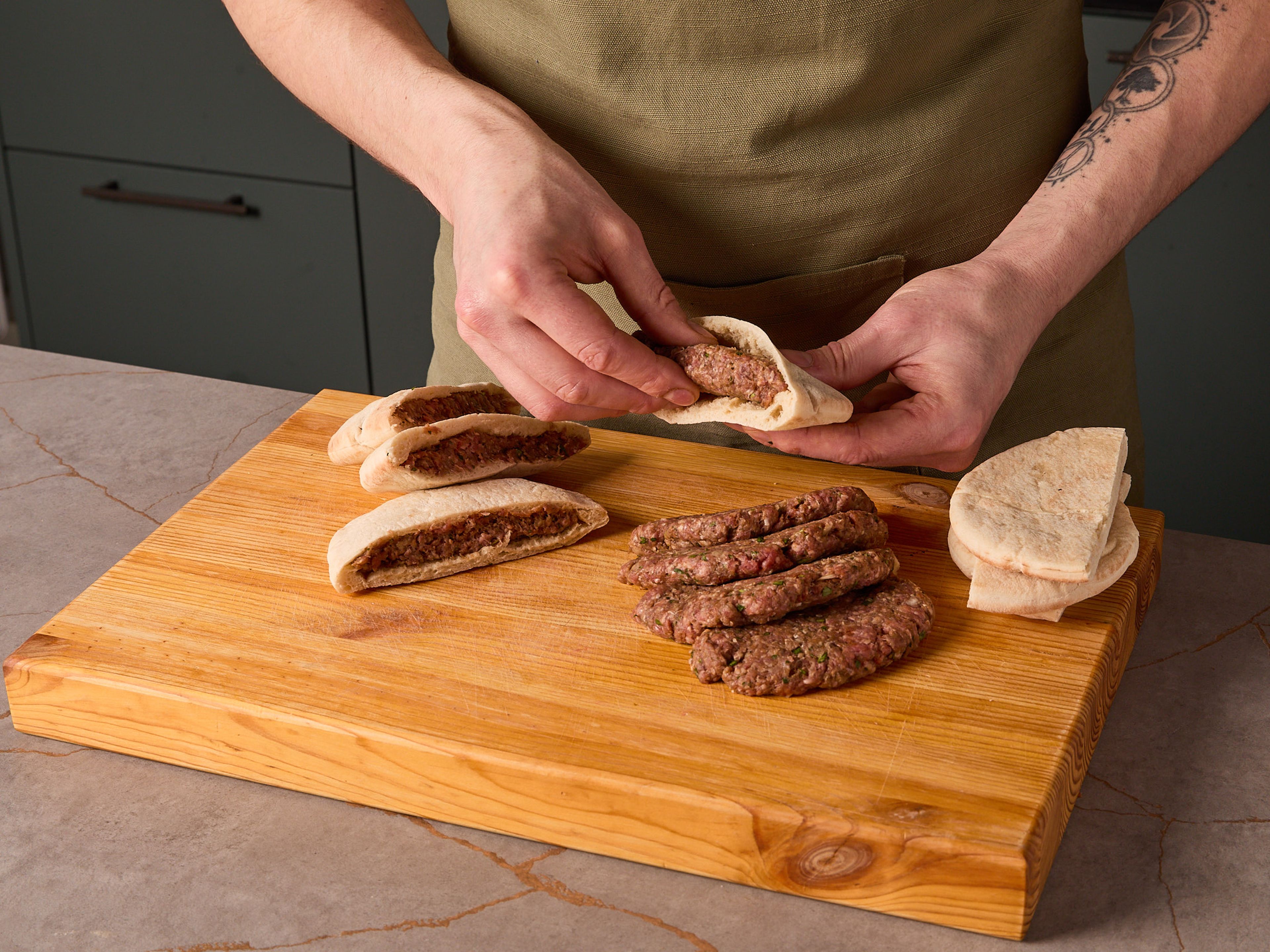 Pita-Brote halbieren und vorsichtig öffnen. Je eine Portion der Fleischfüllung in eine Pita-Hälfte geben, die Taschen schließen und leicht flach drücken, sodass das Fleisch gleichmäßig verteilt ist.