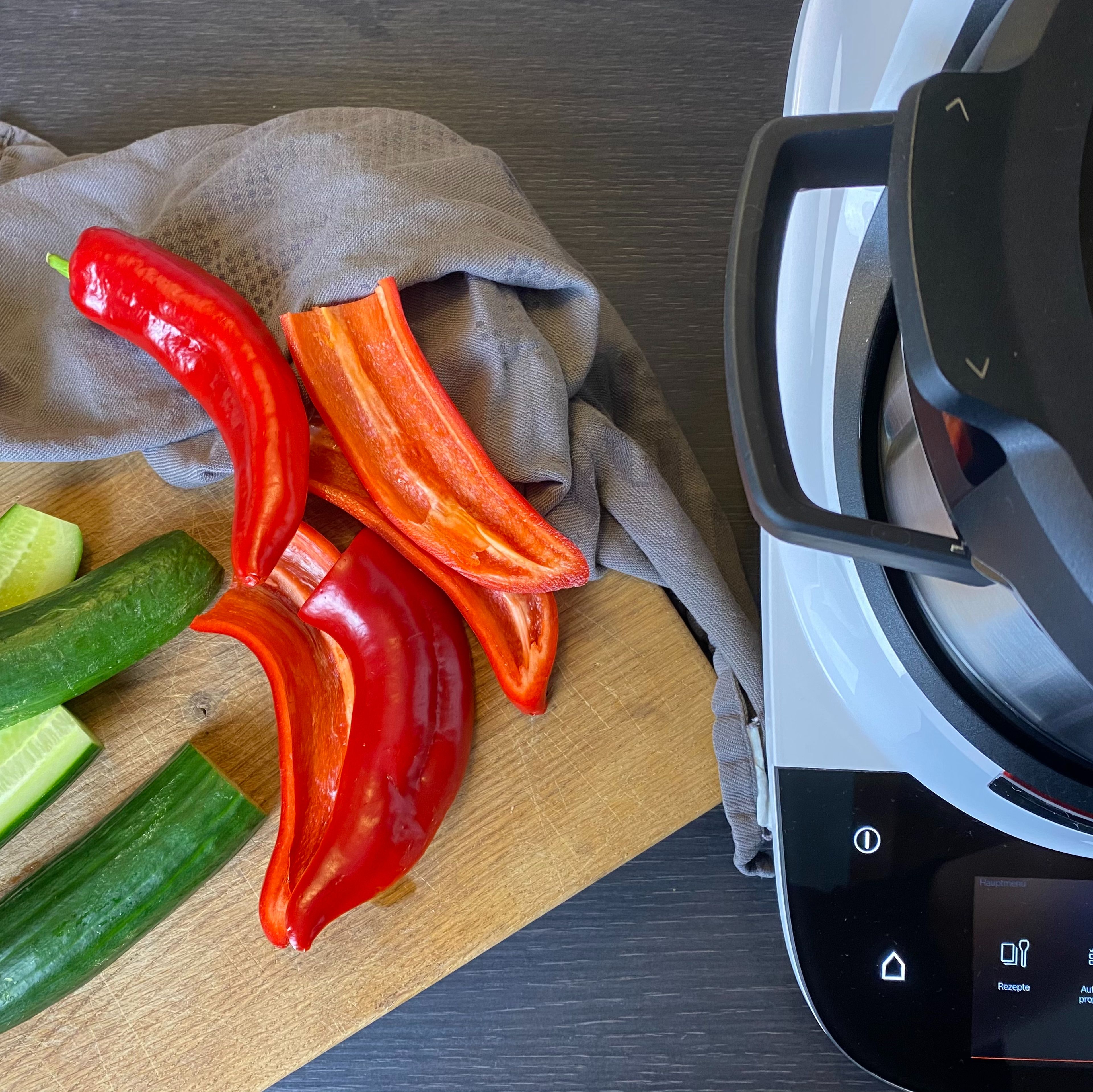 Zuerst die Gurke und Spitzpaprika waschen. Die Gurke nun in der Länge einmal teilen und anschließend längs hälften. Die Paprika entkernen und längs Hälften. Den Zerkleinerungsaufsatz mit der Wendeschneidscheibe, grobe Seite nach oben, einsetzen. Den Deckel schließen und das Gemüse in Stücke bzw. Halbkreise schneiden (Zerkleinerungsaufsatz | Stufe 4).