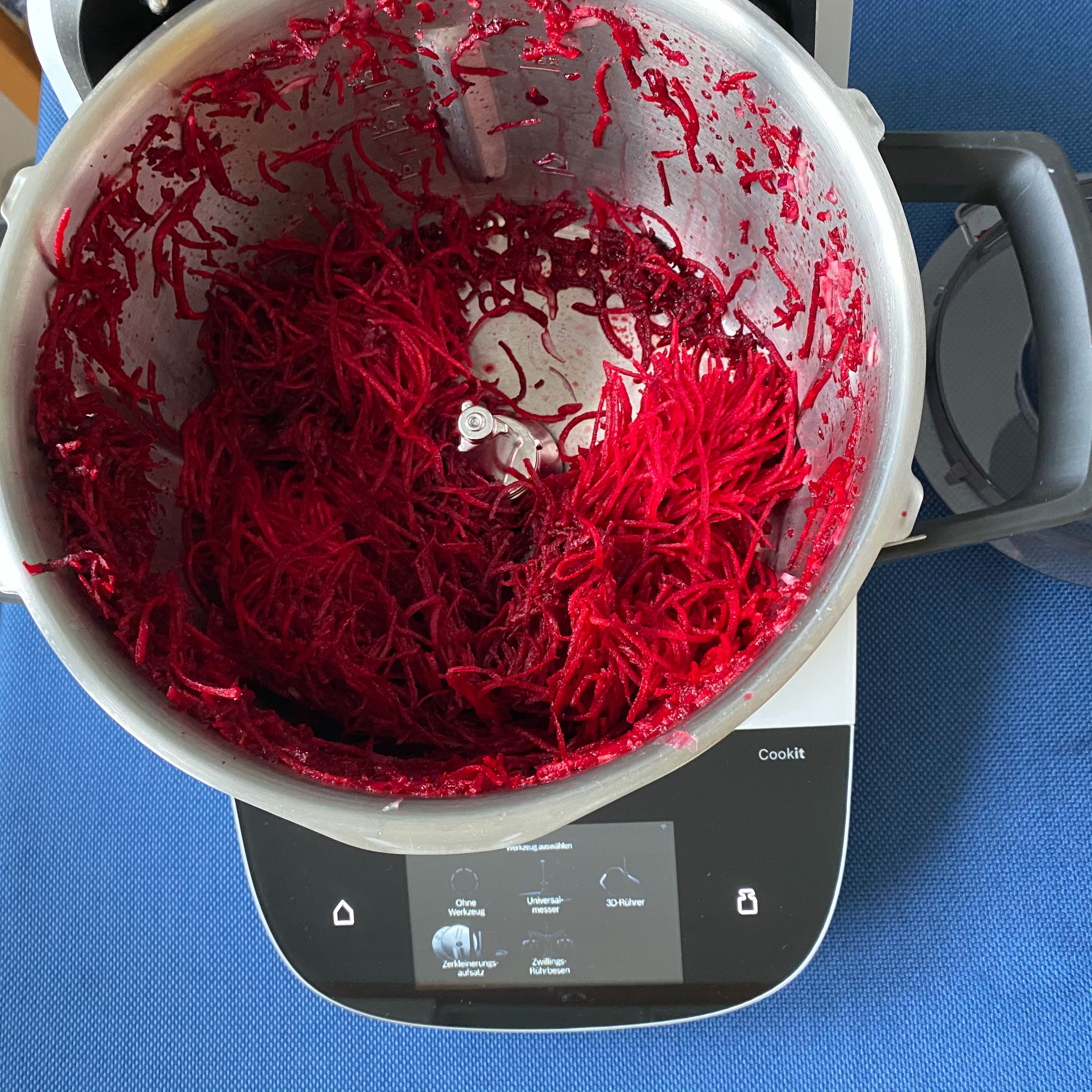Die Cookit Wenderaspelscheibe mit der feinen Seite oben einsetzen, den Deckel schließen, den Messerbecher einsetzen und die rote Bete fein raspeln (Zerkleinerungsaufsatz | Stufe 6). Den Zerkleinerungsaufsatz mit der Raspelscheibe und der Achse entfernen.