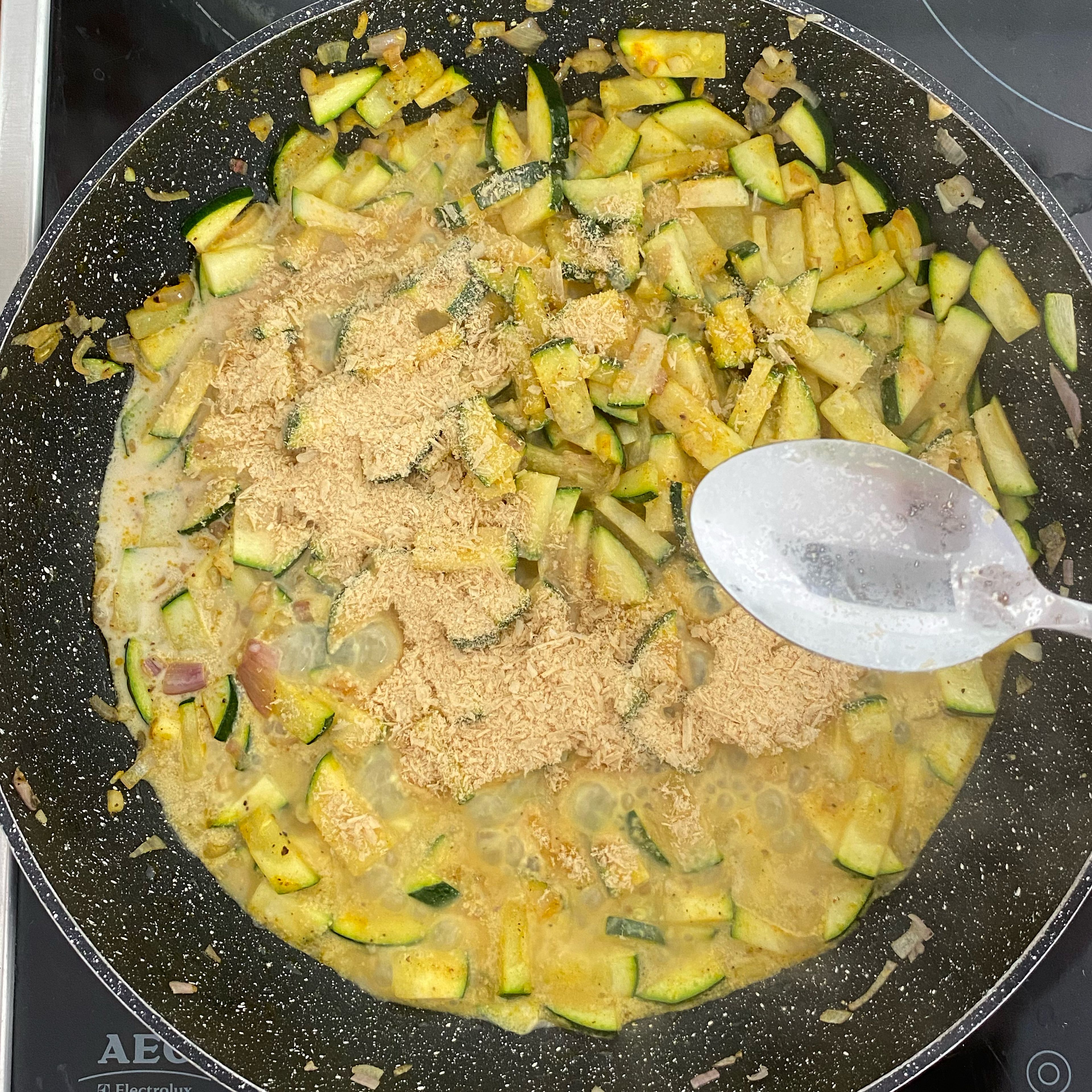 Sobald die Zucchini angebraten ist, alles mit der Milch ablöschen (empfehle Sonnenblumen- oder Hafermilch). Hefe Flocken und Gewürze unterrühren und mit Salz und Pfeffer abschmecken.
