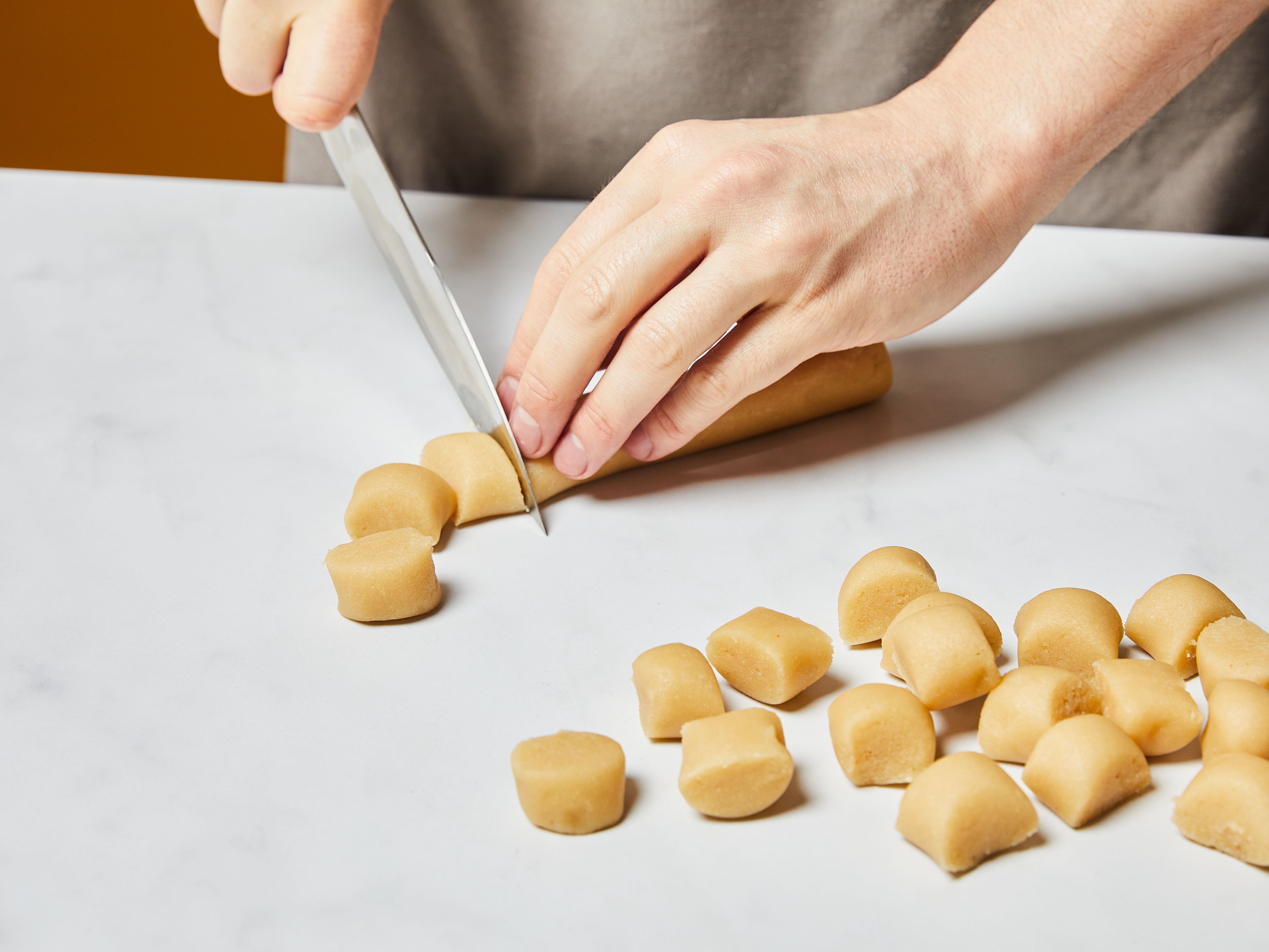 Den Backofen auf 175°C (155°C Umluft) vorheizen. Marzipanrohmasse mit den Händen in kleine Stücke zupfen. Ei trennen und das Eigelb in einer kleinen Schüssel beiseitestellen. Marzipan, Eiweiß, Mehl, Puderzucker, gemahlene Mandeln, Amaretto, Salz und Orangenabrieb (falls verwendet) in eine große Rührschüssel geben und mit den Händen oder einem Handrührgerät zu einem glatten Teig verkneten. Den Teig zu langen Stangen ausrollen und in walnussgroße gleichmäßige Stücke teilen.