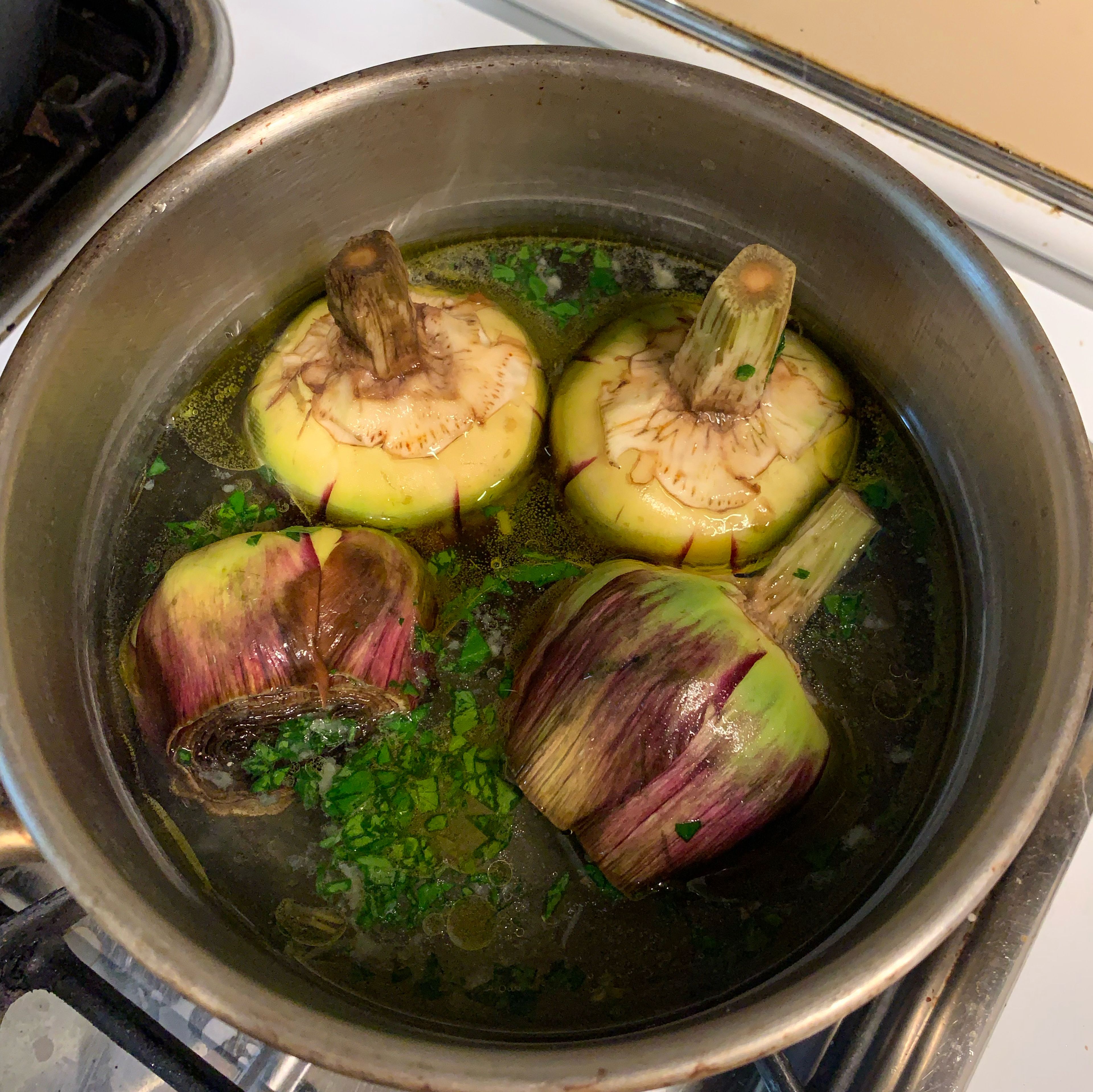 Take a small pan, because we need to keep artichokes pretty close to each other and don't let them fall. Put 4 artichokes heads down in the pan and pour half of the water, then add olive oil and the remaining water. Cover with the lid and over the medium heat let them cook for 30 min. Don't open the lid while it's cooking. After 30 min if you see that the artichokes are a little bit tender, let them simmer for another 5-10 min.
