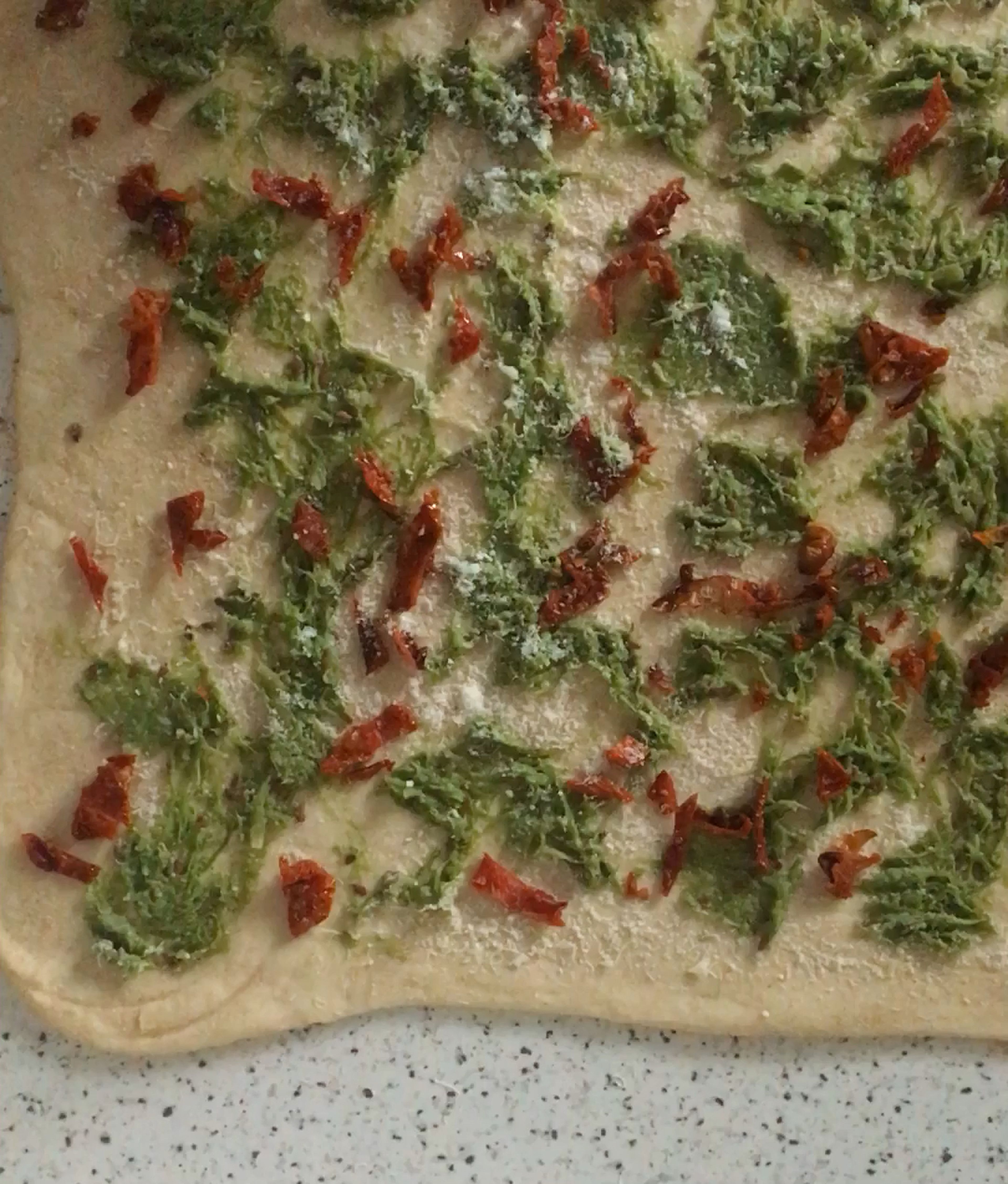 Distribute the spinach pesto, sun-dried tomatoes and remaining Parmesan over the flatten dough.