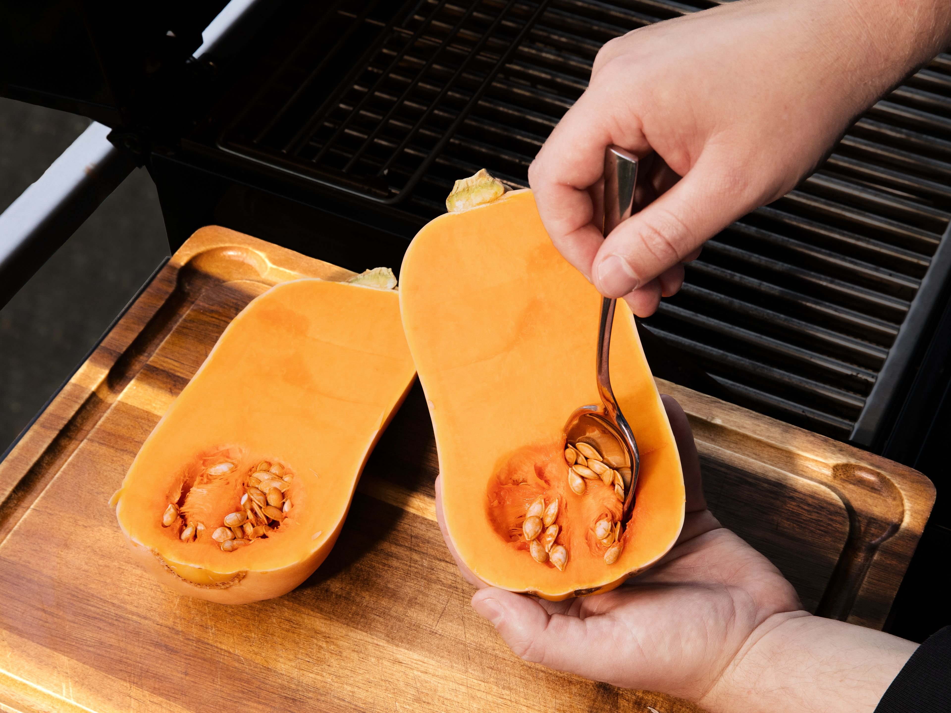 Einen Grill mit Deckel auf mittlere bis hohe Hitze (ca. 200-220 °C) vorheizen. Die Butternut-Kürbisse längs halbieren und mit einem Löffel die Kerne herauskratzen. Knoblauch schälen und fein hacken, Thymianblätter von den Stielen zupfen und ebenfalls fein hacken. Zitrone abreiben, dann halbieren und den Saft auspressen. Für die Marinade etwa die Hälfte des Olivenöls, 2 EL des Zitronensafts, ⅔ des gehackten Knoblauchs, Thymian, 1 TL Zitronenabrieb, Chiliflocken, Salz und Pfeffer verrühren.