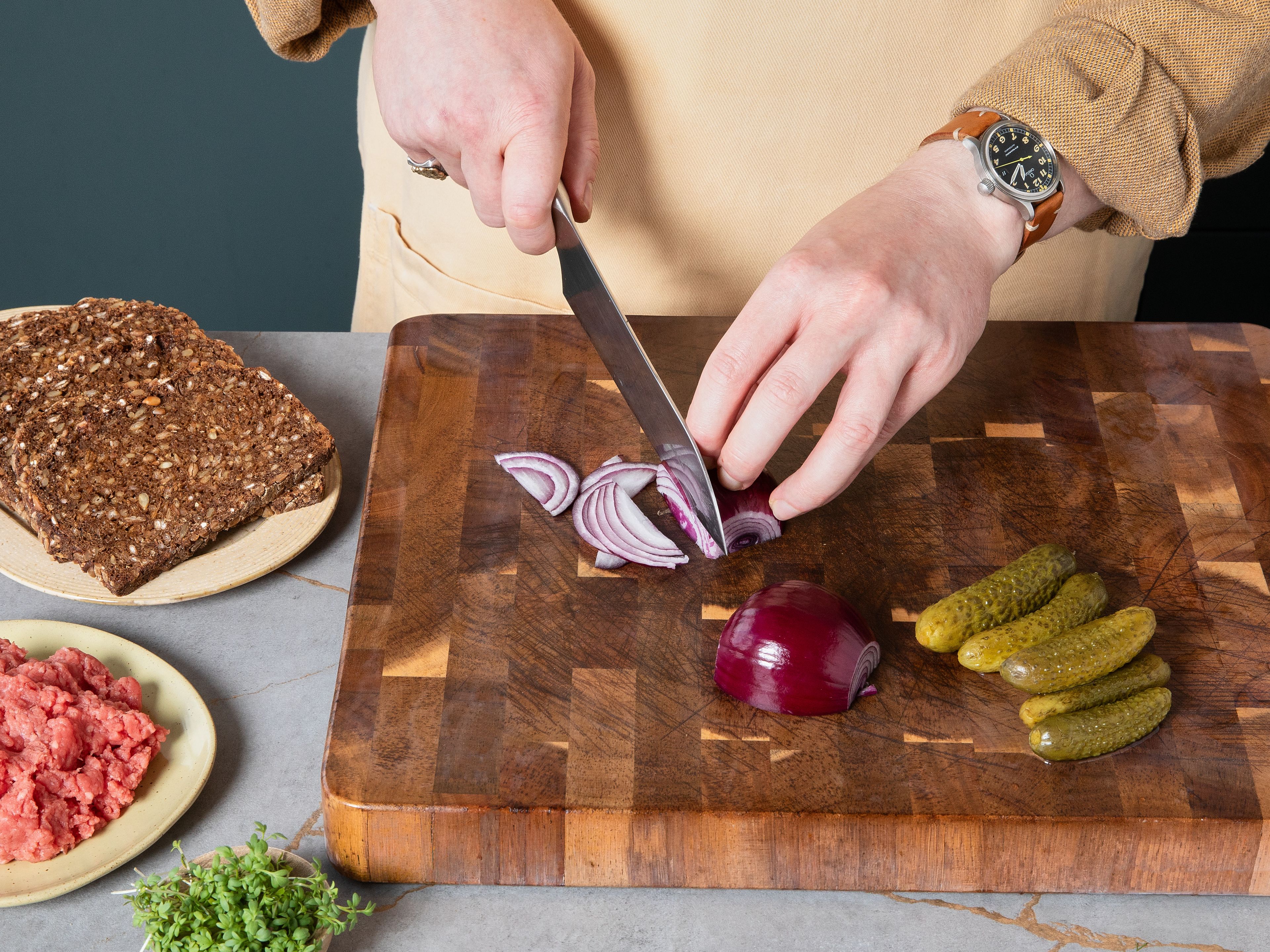 Für das Tatar-Smørrebrød: Bestreiche jede Brotscheibe großzügig mit Butter und verteile anschließend das Tatar gleichmäßig auf beiden Scheiben. Lass dabei in der Mitte jeweils eine kleine Mulde frei, in die später das Eigelb gesetzt wird. Danach mit Salz und Pfeffer würzen. Schneide die Cornichons und die rote Zwiebel der Länge nach in feine, ca. 1 mm dünne Scheiben. Drücke die Cornichons mit der Schnittkante nach unten in das Tatar, sodass sie wellenförmig darin stehen. Verteile dann die Zwiebelscheiben und die Kapern gleichmäßig auf dem restlichen Tatar. Setze den vorbereiteten Meerrettich in mehreren kleinen Tupfen darauf, gib das Eigelb in die Mulde und bestreue zum Schluss alles mit Kresse.