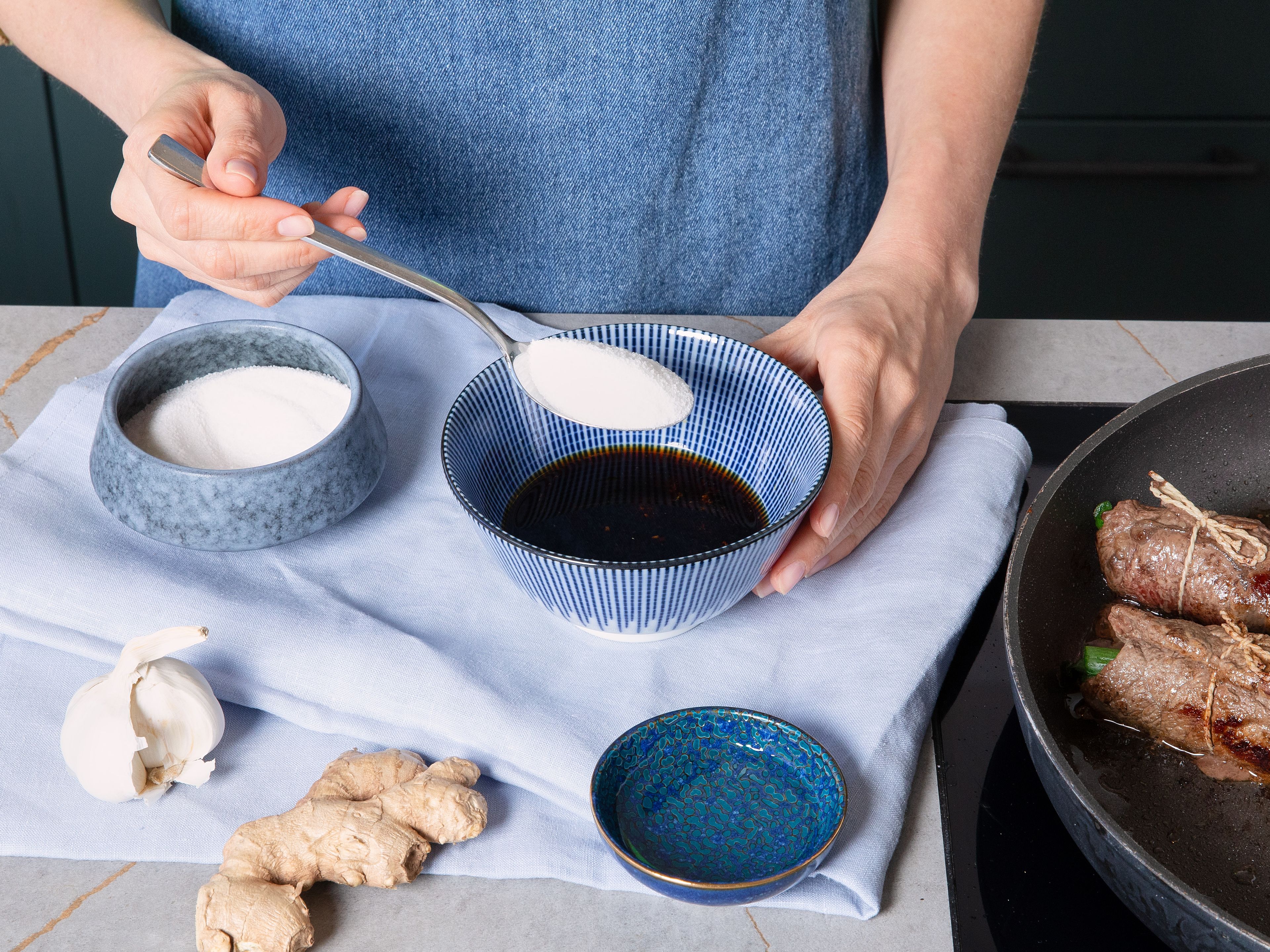 Peel and finely grate ginger and garlic into a small bowl. Add soy sauce, mirin, water, and sugar and stir. Pour sauce into pan and let it reduce briefly until rolls are brilliantly glazed. Remove Negimaki from pan and cut into pieces with a sharp knife. Serve with cooked sushi rice and remaining asparagus. Drizzle with sauce and toasted sesame oil and sprinkle with sesame seeds.