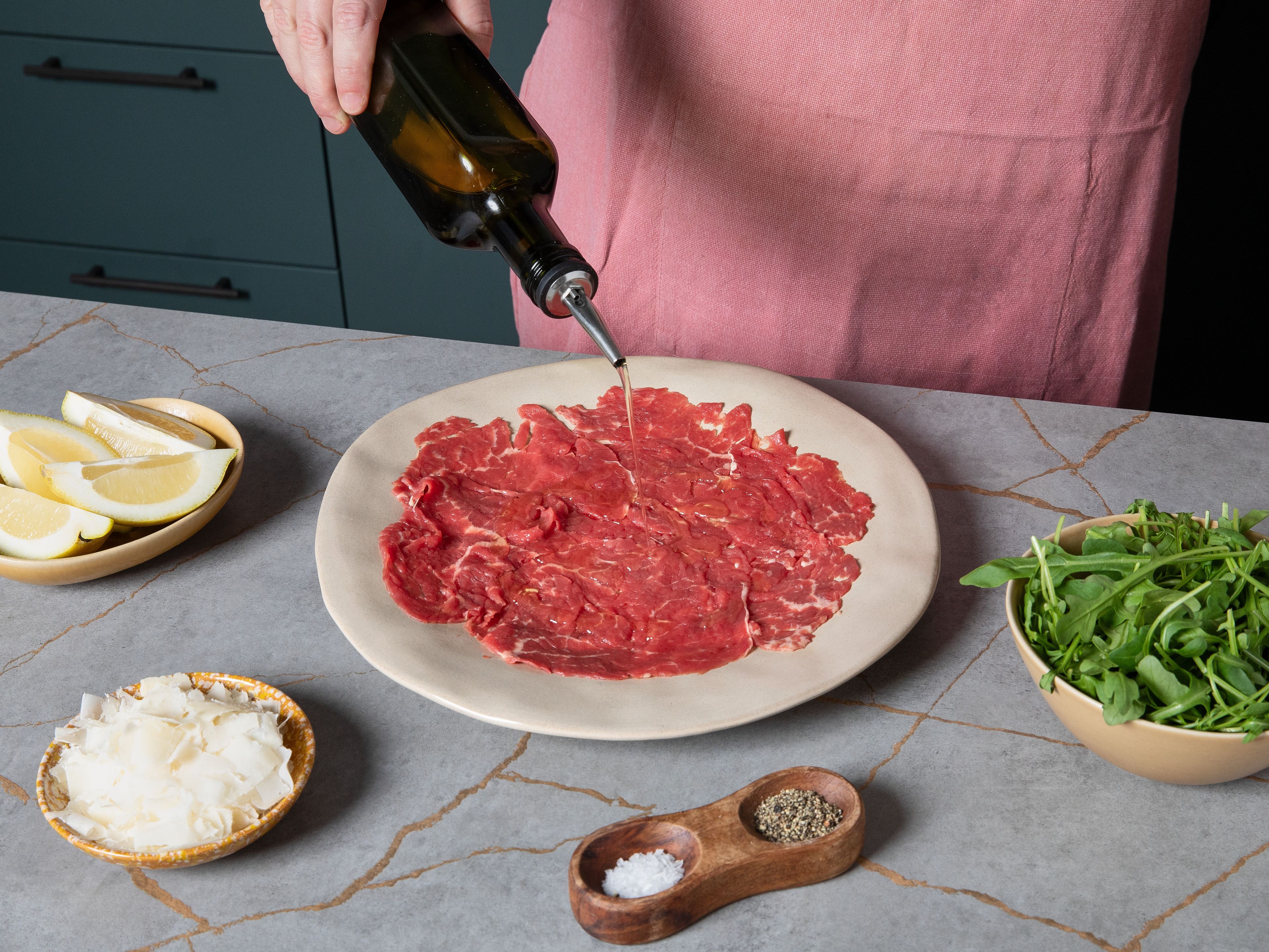 Die obere Folie abziehen und die Fleischscheiben behutsam auf einem großen Teller anrichten. Mit Olivenöl und Zitronensaft beträufeln, mit Rucola bestreuen und Parmesan darüber hobeln. Mit Salz und Pfeffer abschmecken. Nach Beleiben kann das Carpaccio zusätzlich mit etwas Zitronenabrieb verfeinert werden.