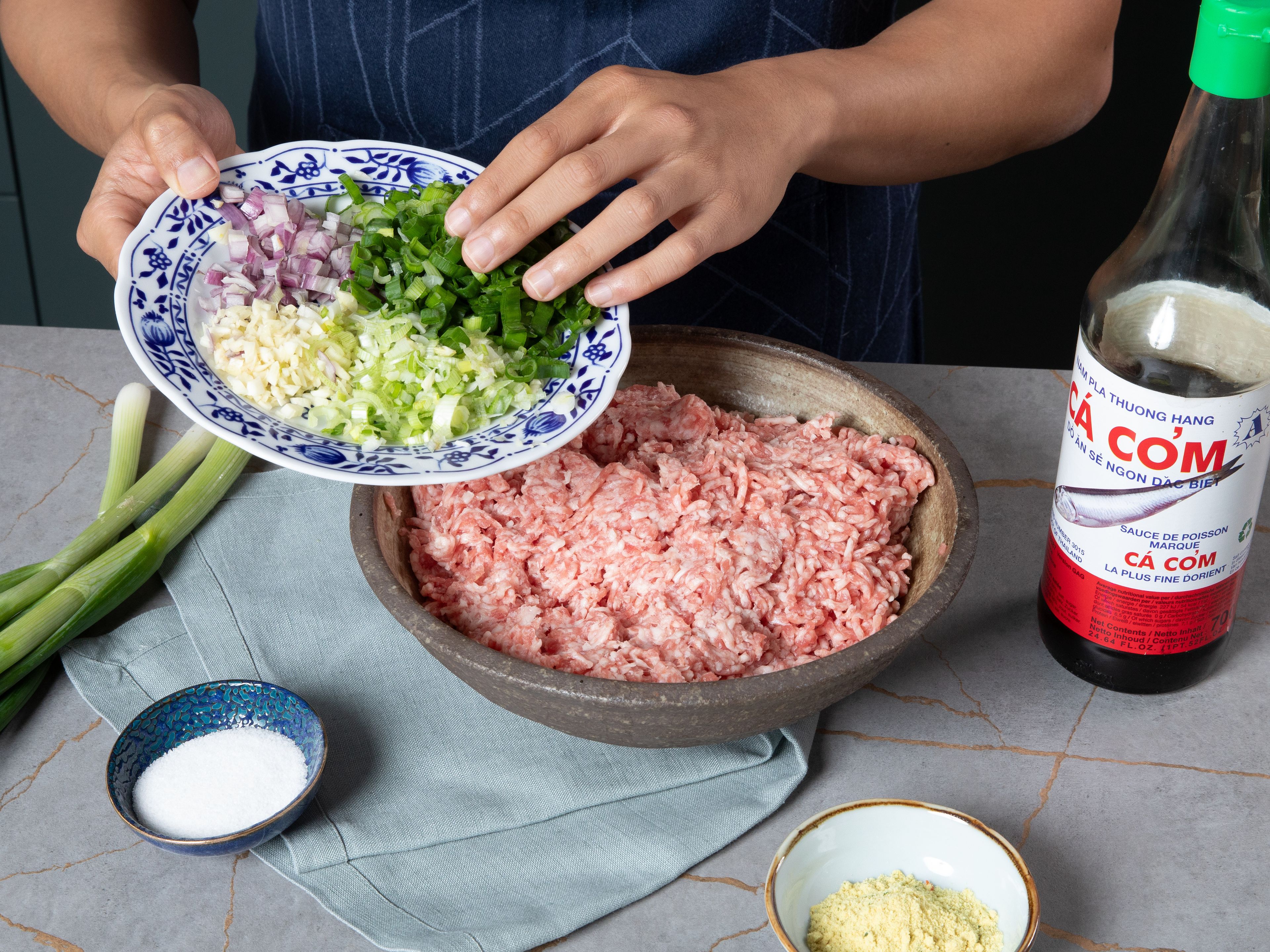 Den Knoblauch und die Schalotte schälen und fein hacken. Dann die Frühlingszwiebel und Thai-Chili in feine Ringe schneiden. Anschließend das Hackfleisch mit einem großen Teil des Knoblauchs, Schalotte, Frühlingszwiebeln, Fischsoße, Zucker, Hühnerbrühe-Pulver und Öl gründlich vermengen. Die Mischung in einer Schüssel beiseitestellen und ca. 30 Min. marinieren lassen (für ein intensiveres Aroma gilt: je länger, desto besser).