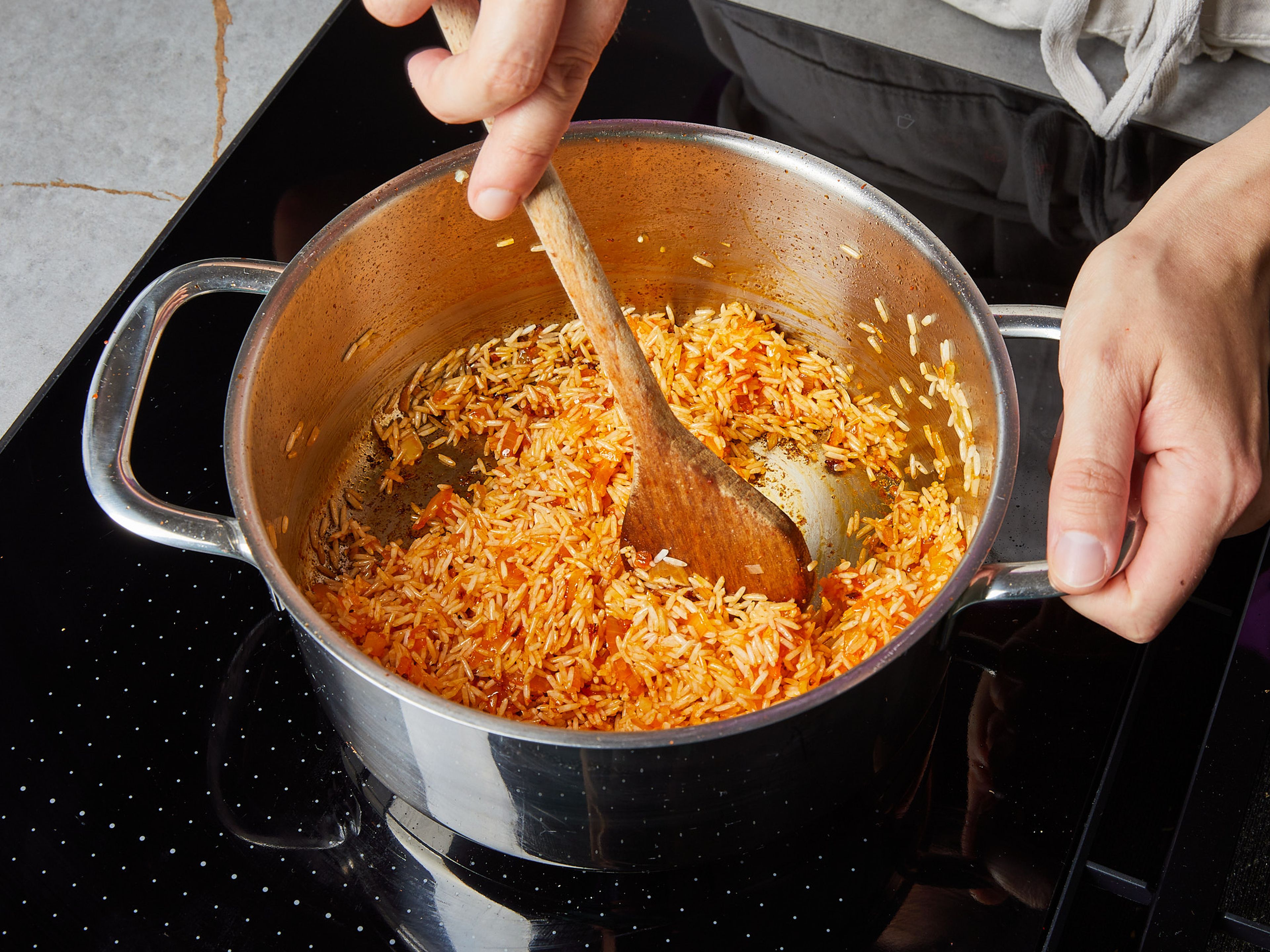 In der Zwischenzeit die Zwiebel würfeln, den Knoblauch hacken und die Minze und Petersilie fein hacken. Den Feta mit den Händen zerbröseln. Das restliche Öl in einem Topf erhitzen, Zwiebel und Knoblauch zugeben und ca. 3 Min. bei mittlerer Hitze anbraten, mit Salz würzen. Harissa zugeben, vermischen und ca. 1 Min. braten. Reis hinzugeben und ca. 2 Min. braten. In der Zwischenzeit die Walnüsse hacken und in den Topf geben.