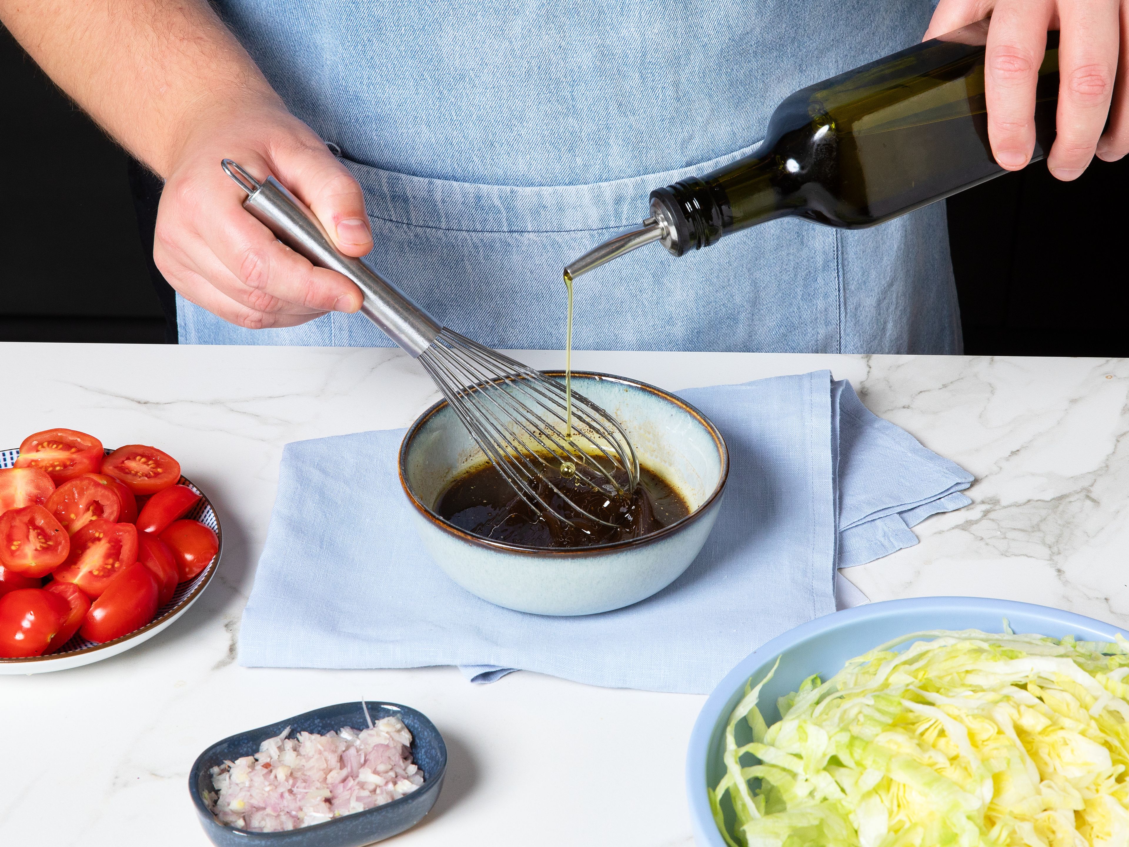 Kirschtomaten halbieren. Den Salat in feine Streifen schneiden. Balsamico-Essig, Honig und Salz in einer Schüssel vermischen. Olivenöl langsam unterrühren, bis ein glattes Dressing entsteht. Tomaten hinzufügen, vermengen und beiseitestellen.