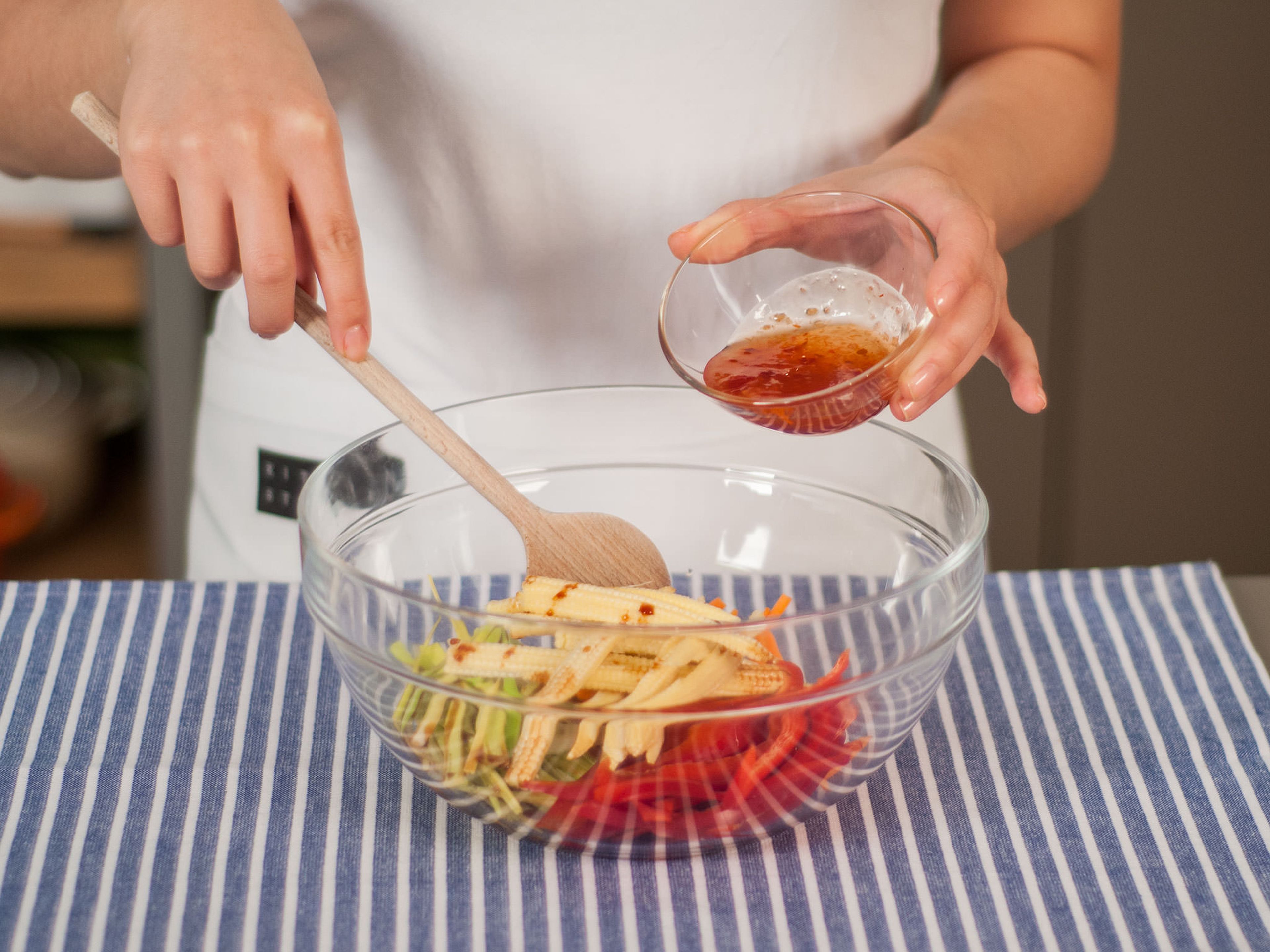 In a large bowl, mix sliced carrots, leek, bell pepper, and baby corn with sweet chili sauce and soy sauce.