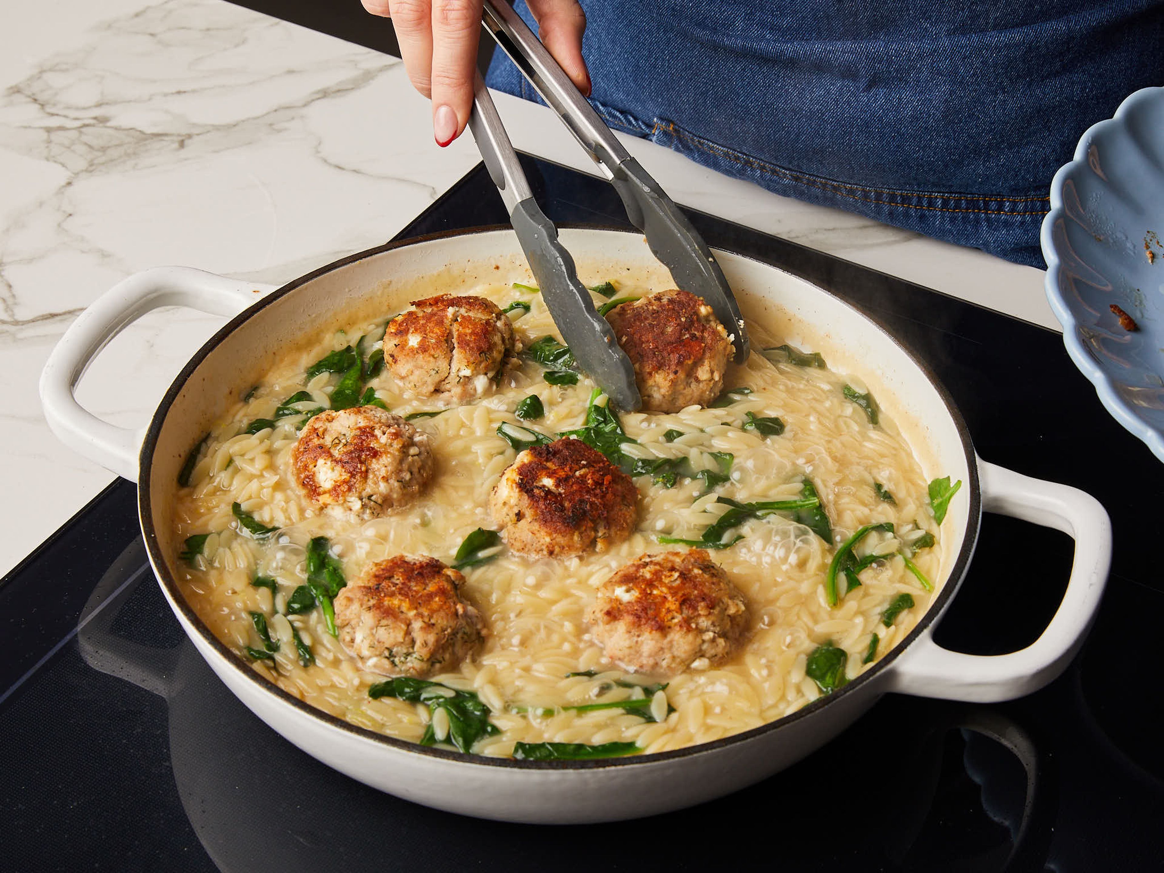 Add lemon zest, juice, salt and pepper to the orzo to taste, stirring well to season. Return meatballs to the pan to gently reheat them. Slice your remaining lemon into wedges. Sprinkle dill, remaining feta and lemon wedges to serve.