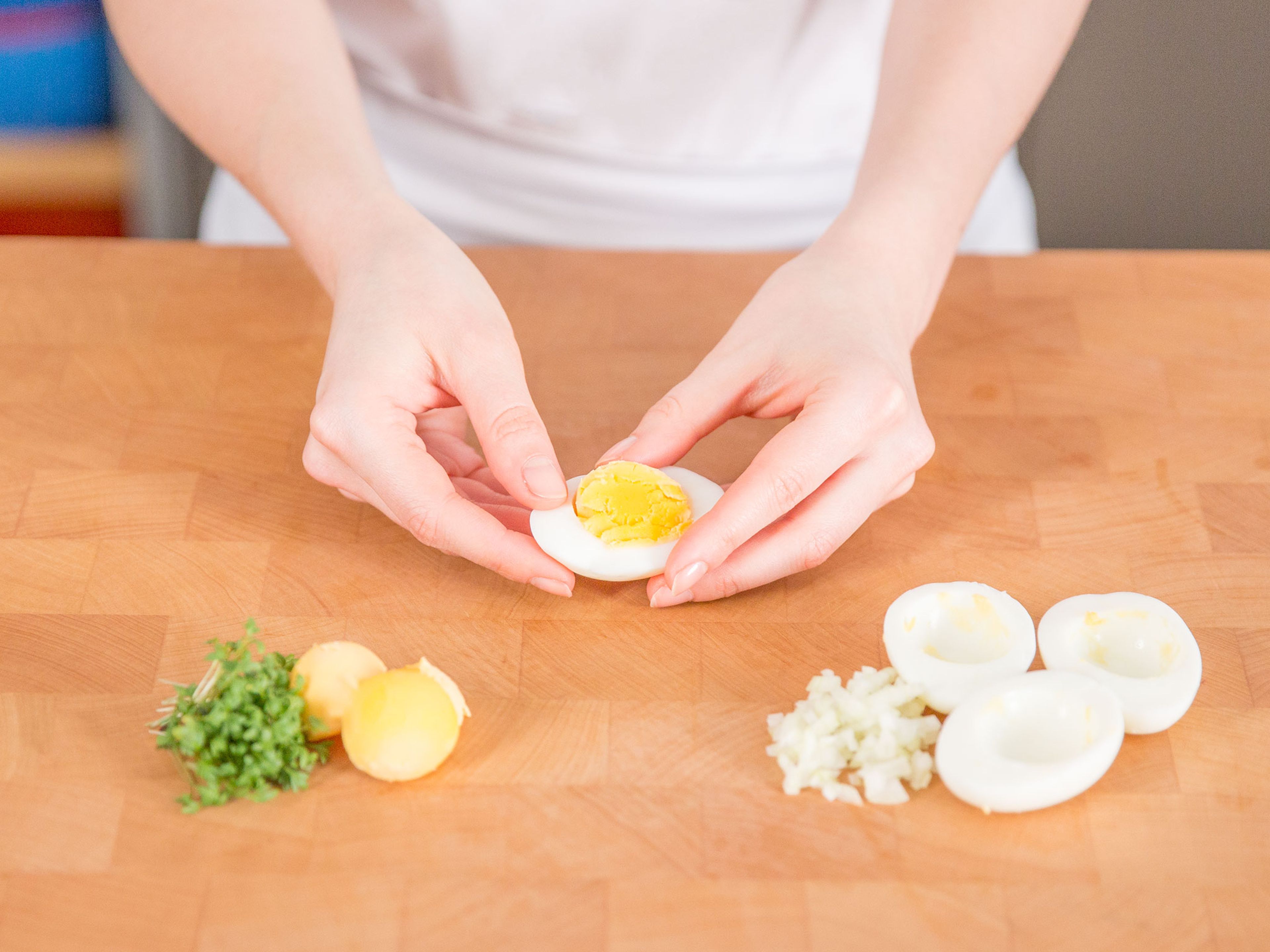 Wasser in einem kleinen Topf zum Sieden bringen. Eier für ca. 8 - 10 Min. kochen, dann mit kaltem Wasser abschrecken. Eier schälen und längs halbieren, dann von jeder Eihälfte eine kleine Scheibe unten abschneiden, damit sie nicht umfallen. Eigelbe mit einem Löffel entfernen, beiseite stellen. Zwiebel fein hacken.